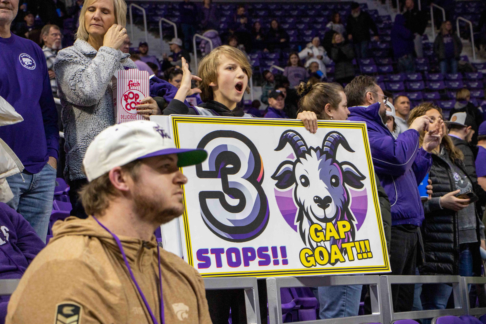 A fan flashing a Wildcat holds a Gap Goat sign. Gappy, the women's basketball team's unofficial mascot, is held up by a team manager for every three stops the K-State defense gets.