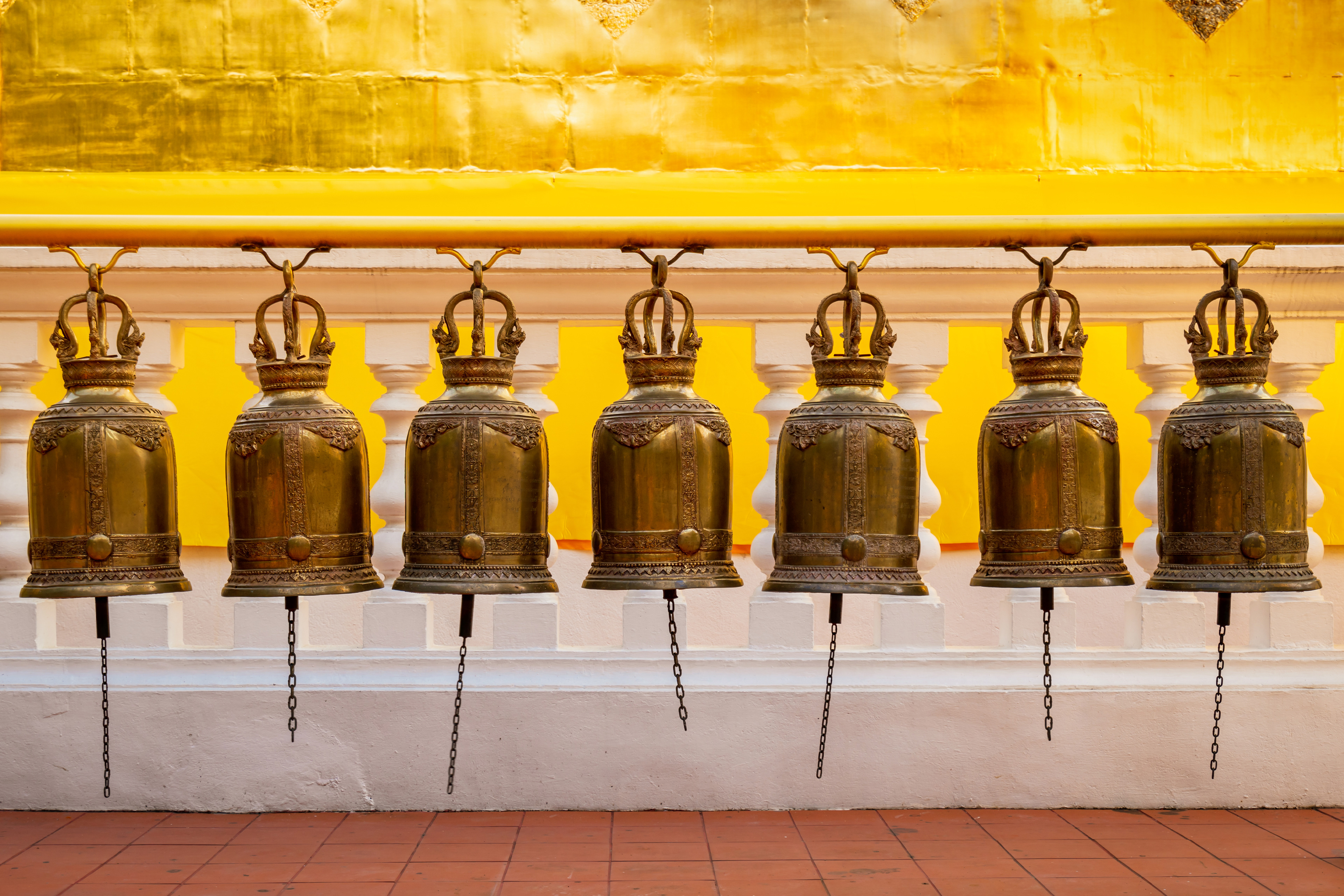 Thailand the “Land of Smiles,” has become one of our favorite travel destinations in Asia over the last few years. It has the perfect balance. Prayer bells in a row against a yellow temple wall.
