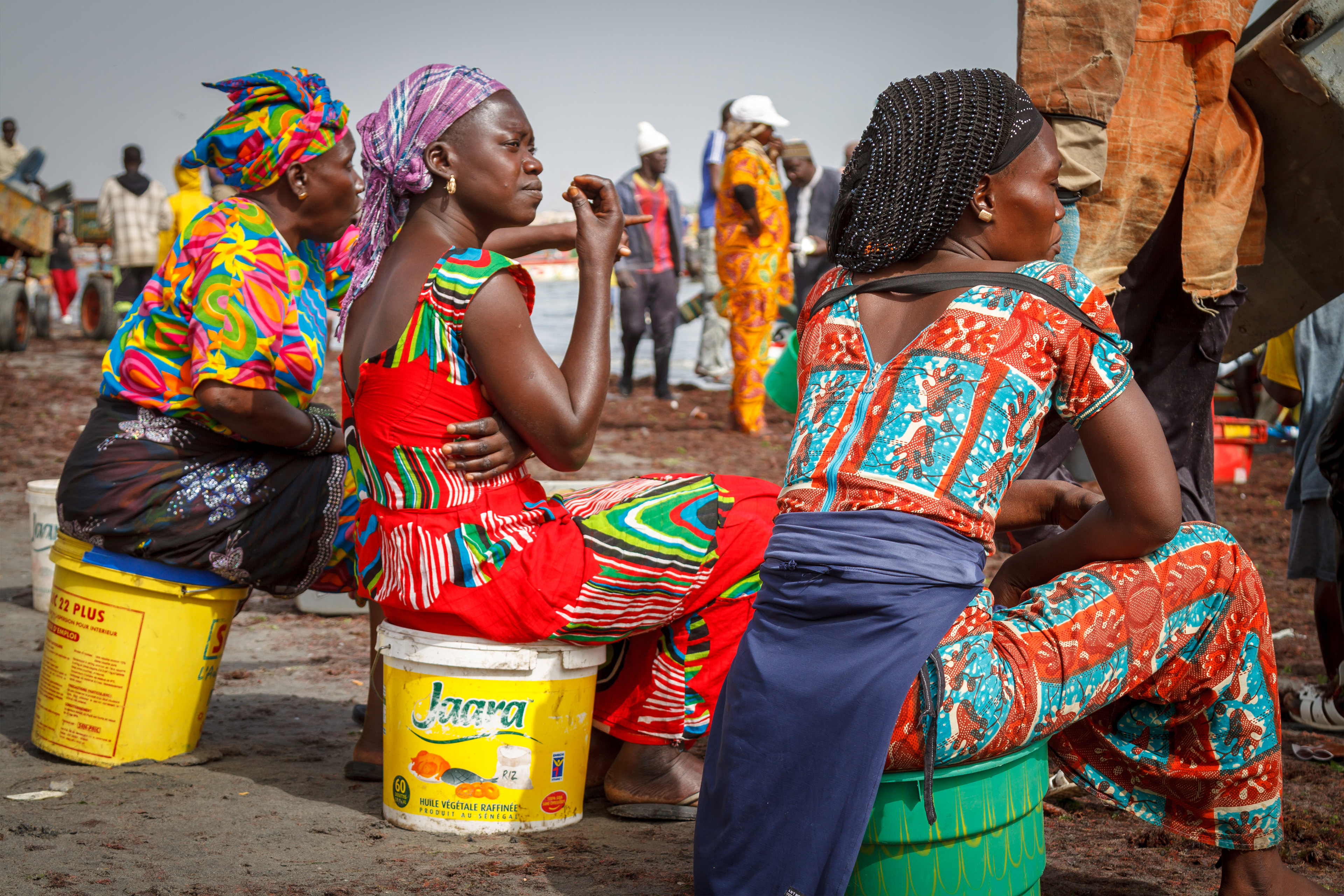 Women in colourful traditional dress waiting for the daily fish catch to arrive.