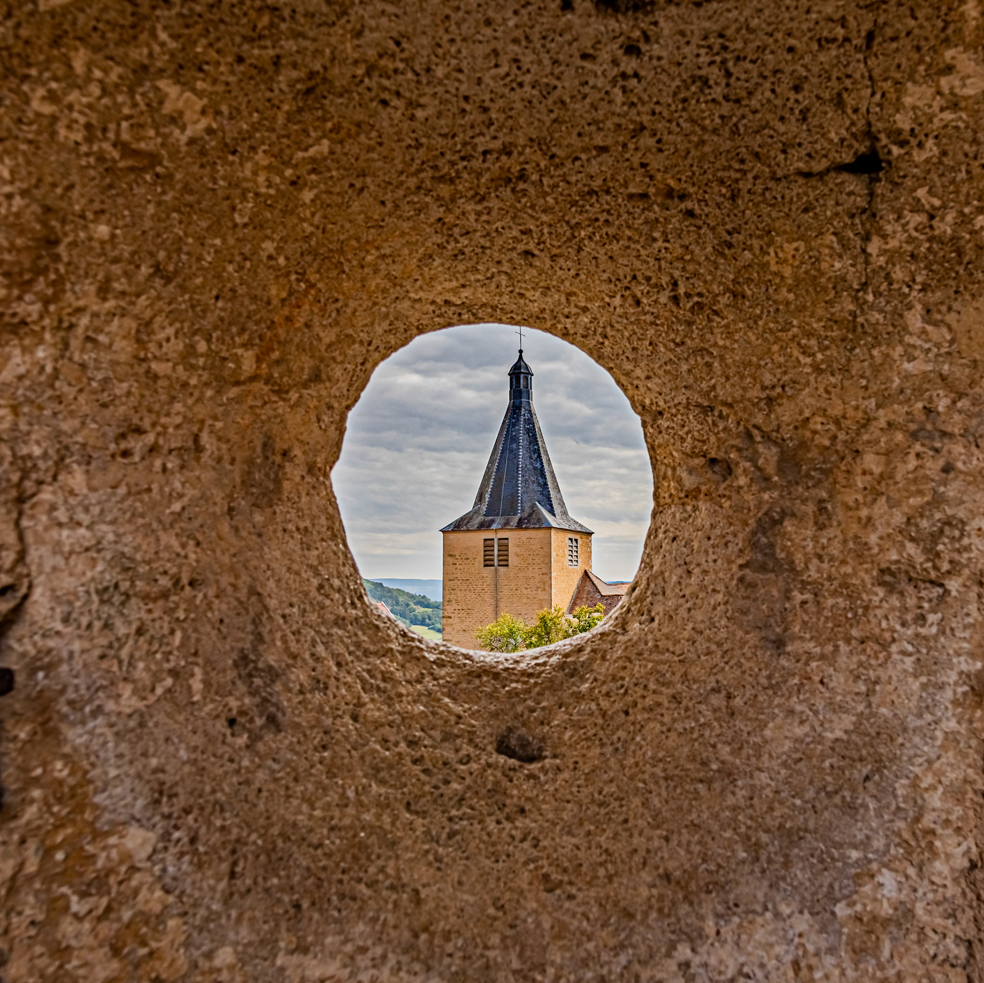 L'église de Saint-Philippe et Saint-Jacques de Châteauneuf-en-Auxois vue à travers un trou dans l'enceinte du château.