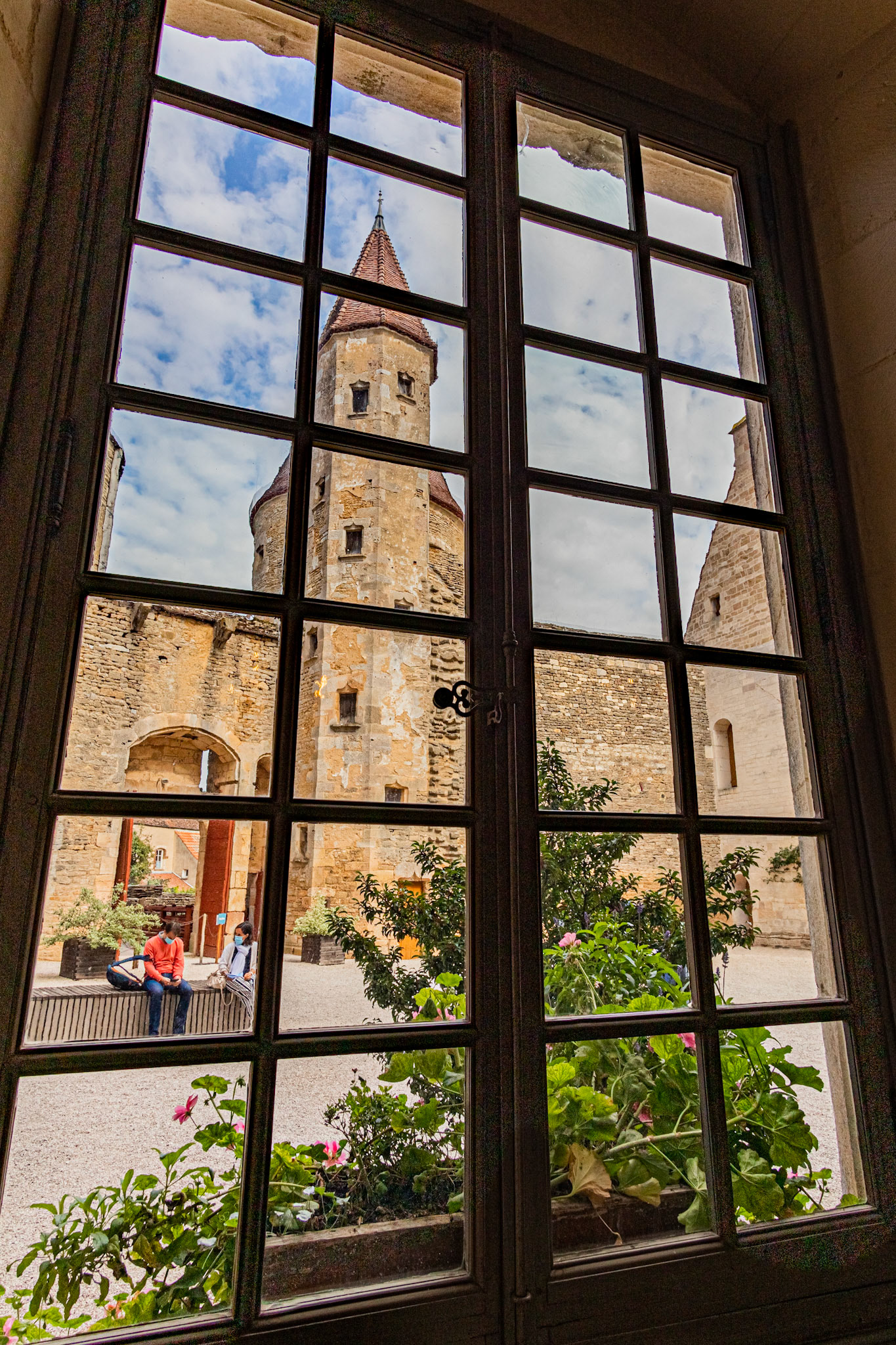 Vue sur la cour du château de Chateauneuf-en-Auxois et sa tour, à travers une grande fenêtre.