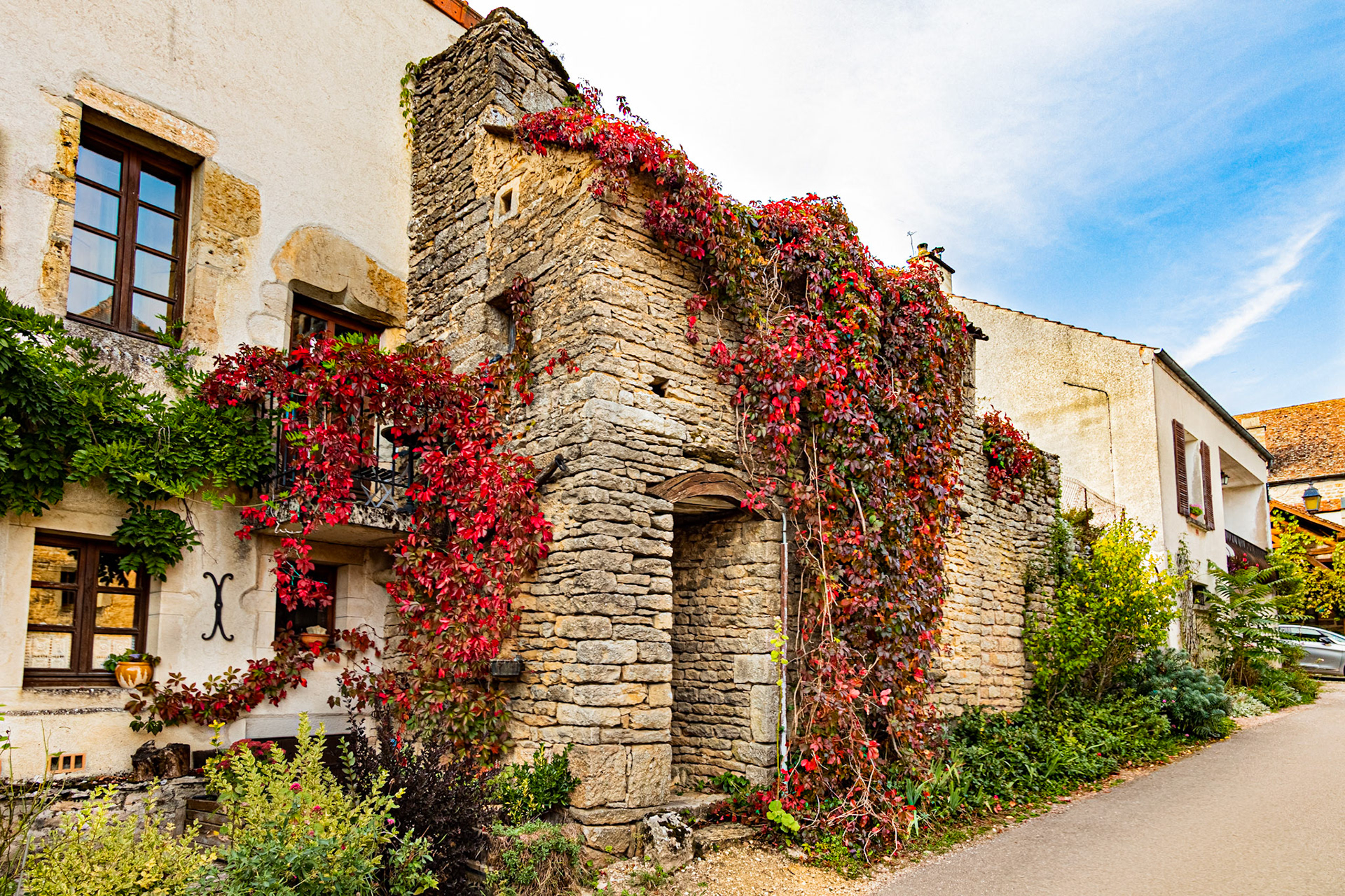 Vieille maison en pierre à Châteauneuf-en-Auxois, partiellement recouverte de feuilles aux couleurs rouge de l'automne.