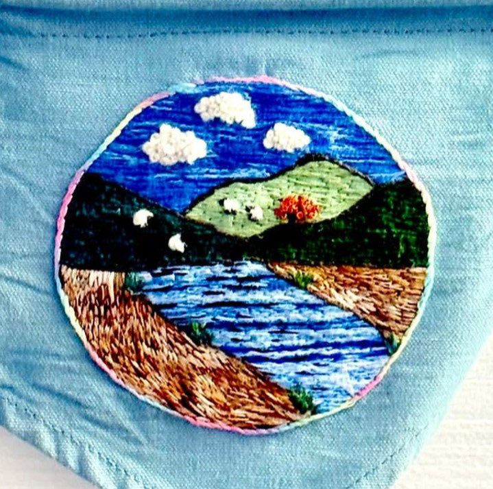 “A view from Rainbow's End” Laura (fLaura & fauna healing stitches), hand embroidery, 2025 “In the summer of 2025, I was unwittingly getting closer and closer to burnout. Years of being stuck in fight or flight was slowly chipping away at my functioning, my mood and my work-life balance.  I didn't recognise it, but my brain and nervous system were in overdrive. I'd desperately search for things to help with the overwhelm and anxiety, often trying hobby after hobby, but never being able to stick to anything or find anything that really helped.  I had bought a basic embroidery kit that summer, as another attempt at trying to calm my poor brain, and for some reason when I started that simple kit, my brain felt like it was being told it was safe.  Since then, I have developed my skills and started going to a weekly stitching group, and it's quite frankly saved my life.  In October, just a few months after discovering embroidery, a friend had his life turned upside down when he had a stroke at age 47. My nervous system was yet again on high alert, remembering the feelings of previous trauma, except this time, I could turn to embroidery. He owns a boat called Rainbow's End, which is a floating haven of calm, so whilst he was in hospital trying to recover his life and function back, I started this piece. By the time it was ready, it was perfect for his Christmas present, and represents my solace during those 3 months, his progress, and is the calm pot of gold at the end of the rainbow.  I'd love to help show you that even when your brain is struggling, busy, stuck in fight or flight, or always on the go from past trauma, that healing can start from just a needle and thread.” @flaurafaunahealingstitches