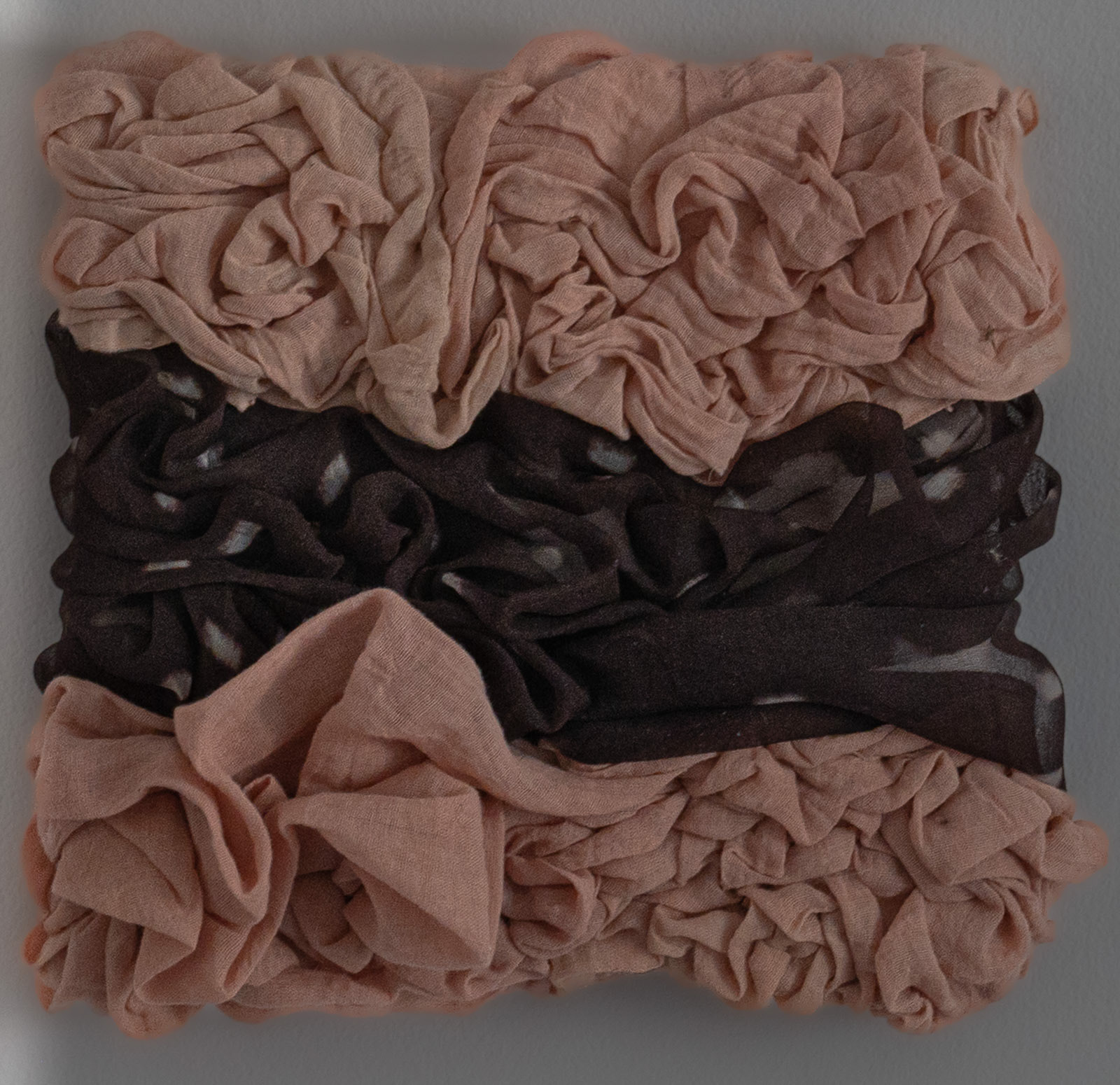 “Retention: Band” Elizabeth Benson, Textile, 2026 “Retention: Band is a sculptural textile work created from naturally dyed butter muslin and silk organza. Dyed with madder root, iron, alkaline modifiers and resist processes, the fabrics are compressed into horizontal bands where tension fixes the cloth into dense folds. The work explores the relationship between softness and restraint, transformation and permanence. Colour, compression and gravity become collaborators in the making process, leaving the textile to hold a visible record of its own manipulation. The resulting form balances vulnerability with structure, inviting close attention to the subtle shifts of surface, material and light.” www.elizabethbensonart.com or instagram @elizaabenson 