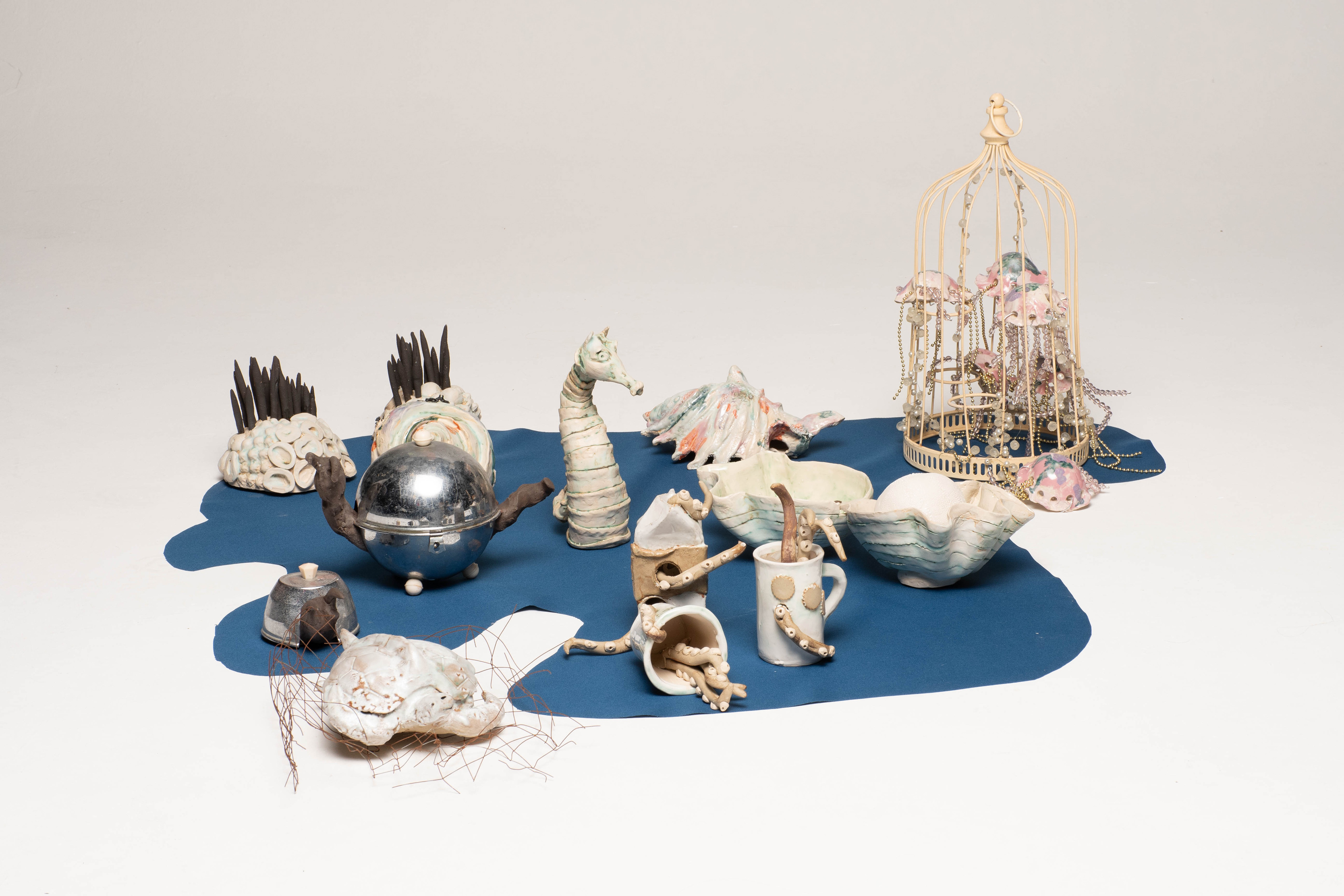 “Shed Salty Tears” Helen Birnbaum, Ceramic and reclaimed media, 2023 “In 2023, 480,343 pieces of litter were found on UK beaches, by 2024 this had become 764,451.. The fish, marine animals and birds that become caught in plastic rubbish suffocate, stave and drown: hundreds of marine species have been harmed by the debris we leave in our oceans. As our planet faces greater and greater environmental problems I strive to create work that combines important ecological messages alongside sustainable practice. Shed Salty Tears draws attention to the bleaching of the sea bed and pollution and consists of many ceramic pieces which are integrated with found objects.  Calling us to take notice of this environmental crisis is the statue of a woman at the centre of the ceramic installation Shed Salty Tears; the voice of the planet, calling us to notice the state of our environment degraded by industrialisation. Crushed cans, rusty metal forms and discarded plastic cluster around the central sculptures. Reclaimed materials challenge viewers to consider what they consume and how it is discarded.  Shed Salty Tears is a triptych with each of the three separate sections having their own particular emphasis. Each section has approximately fifty white, grey and blue shells, corals and other sea life surrounding three large central sculpted figures; a telephone; an African harp and a crying figure shedding salty tears. In striking contrast brightly coloured ceramic made red, orange and green drinks cans, milk bottles and baked bean cans suggest the detritus causing damage to our seas and beaches.  Shed Salty Tears also includes a selection of bizarre sea creatures envisaged as part organic and part metal debris suggesting that because of the rubbish we throw into the sea this is what the creatures might even become - part organic matter and part the rubbish we humans have left behind.” helenbirnbaumceramics.com  @helenbirnbaumceramics