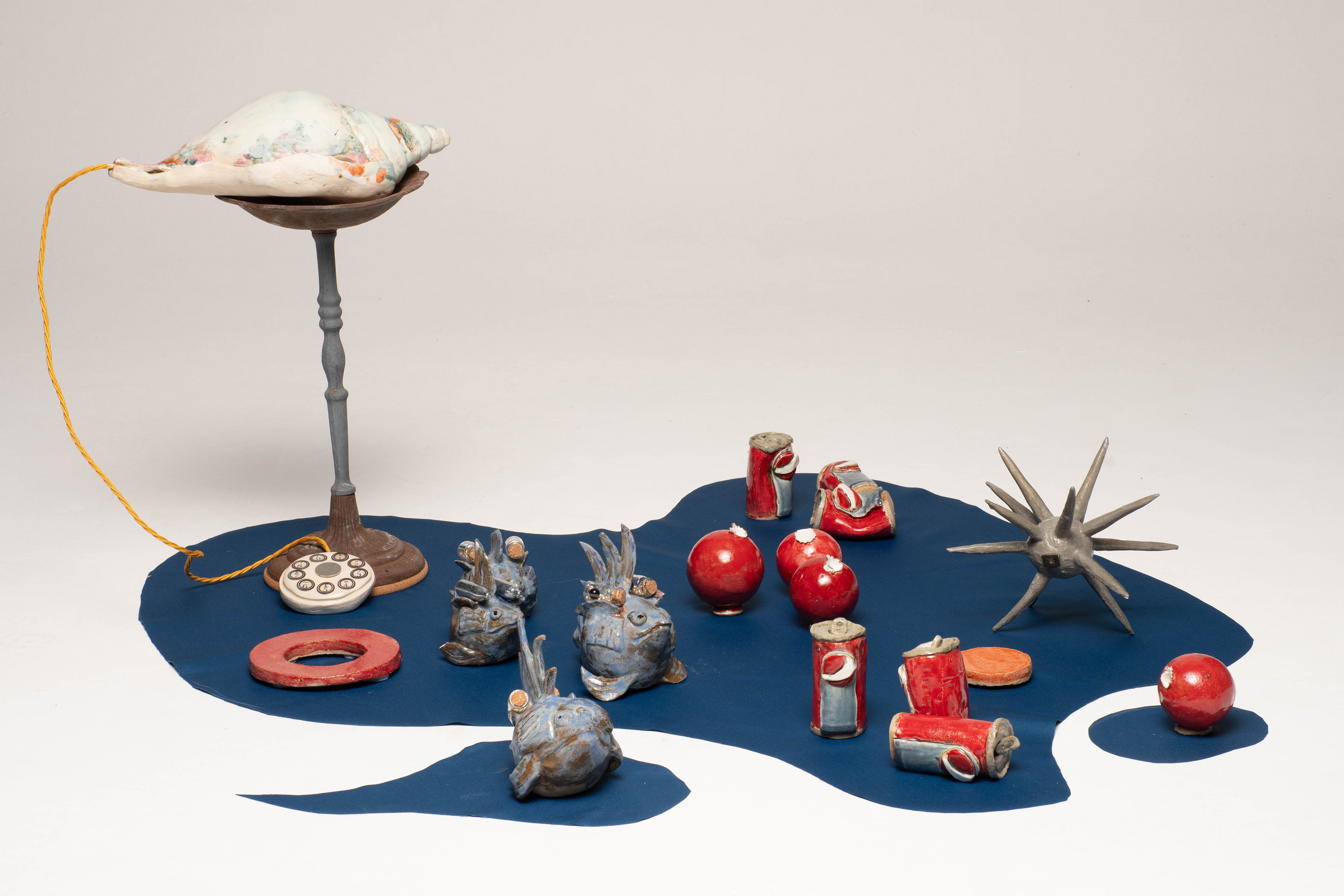 “Shed Salty Tears” Helen Birnbaum, Ceramic and reclaimed media, 2023 “In 2023, 480,343 pieces of litter were found on UK beaches, by 2024 this had become 764,451.. The fish, marine animals and birds that become caught in plastic rubbish suffocate, stave and drown: hundreds of marine species have been harmed by the debris we leave in our oceans. As our planet faces greater and greater environmental problems I strive to create work that combines important ecological messages alongside sustainable practice. Shed Salty Tears draws attention to the bleaching of the sea bed and pollution and consists of many ceramic pieces which are integrated with found objects.  Calling us to take notice of this environmental crisis is the statue of a woman at the centre of the ceramic installation Shed Salty Tears; the voice of the planet, calling us to notice the state of our environment degraded by industrialisation. Crushed cans, rusty metal forms and discarded plastic cluster around the central sculptures. Reclaimed materials challenge viewers to consider what they consume and how it is discarded.  Shed Salty Tears is a triptych with each of the three separate sections having their own particular emphasis. Each section has approximately fifty white, grey and blue shells, corals and other sea life surrounding three large central sculpted figures; a telephone; an African harp and a crying figure shedding salty tears. In striking contrast brightly coloured ceramic made red, orange and green drinks cans, milk bottles and baked bean cans suggest the detritus causing damage to our seas and beaches.  Shed Salty Tears also includes a selection of bizarre sea creatures envisaged as part organic and part metal debris suggesting that because of the rubbish we throw into the sea this is what the creatures might even become - part organic matter and part the rubbish we humans have left behind.” helenbirnbaumceramics.com  @helenbirnbaumceramics