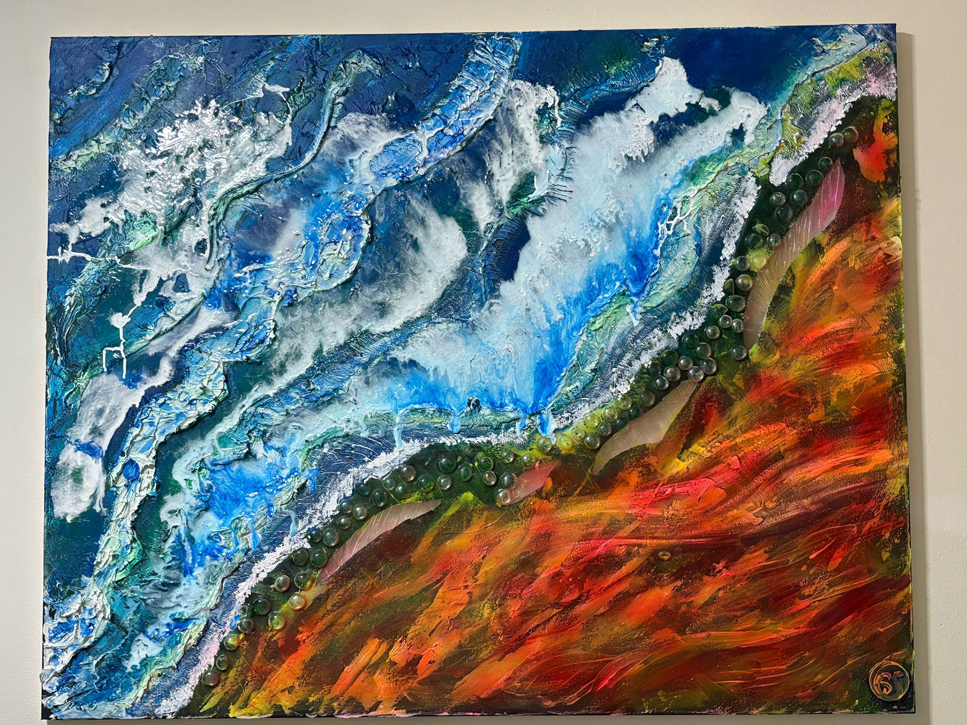 “Burning Tide” Gaby Salvi, mixed media acrylic, 2026 “This abstract mixed-media piece captures the tension between opposing forces — water and fire, calm and destruction, softness and power. Flowing oceanic blues crash against fiery, textured earth tones, creating a dramatic boundary where transformation takes place. The layered textures and embedded elements evoke movement, erosion, and resilience, suggesting that beauty can emerge from conflict and instability