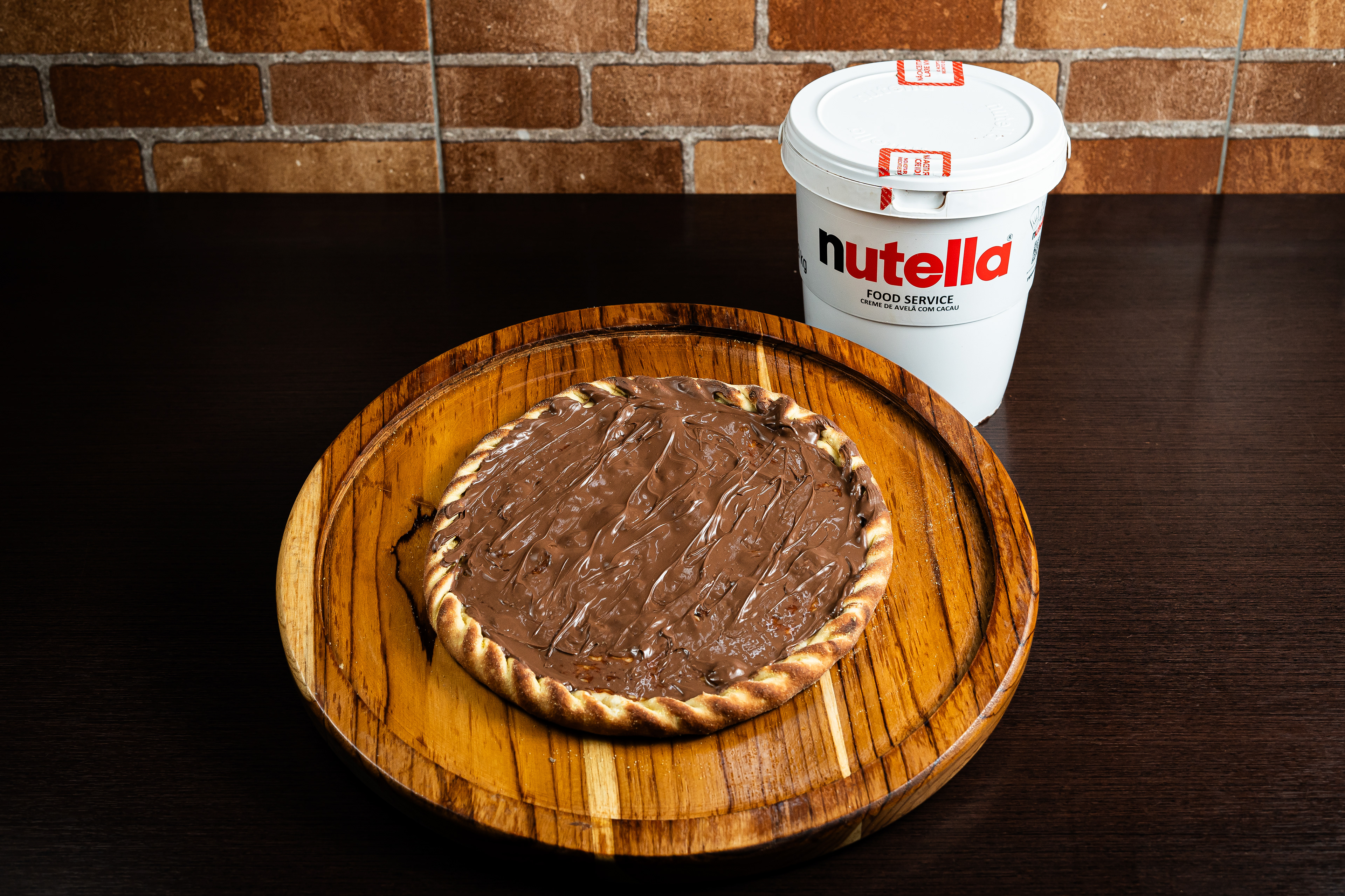 Uma cena que ilumina até os dias mais cinzentos: nossa pizza de Nutella chocolate ao lado de um pote tentador de Nutella. Prepare-se para uma explosão de sabor e felicidade! 🍫✨ #IluminandoComSabor"
