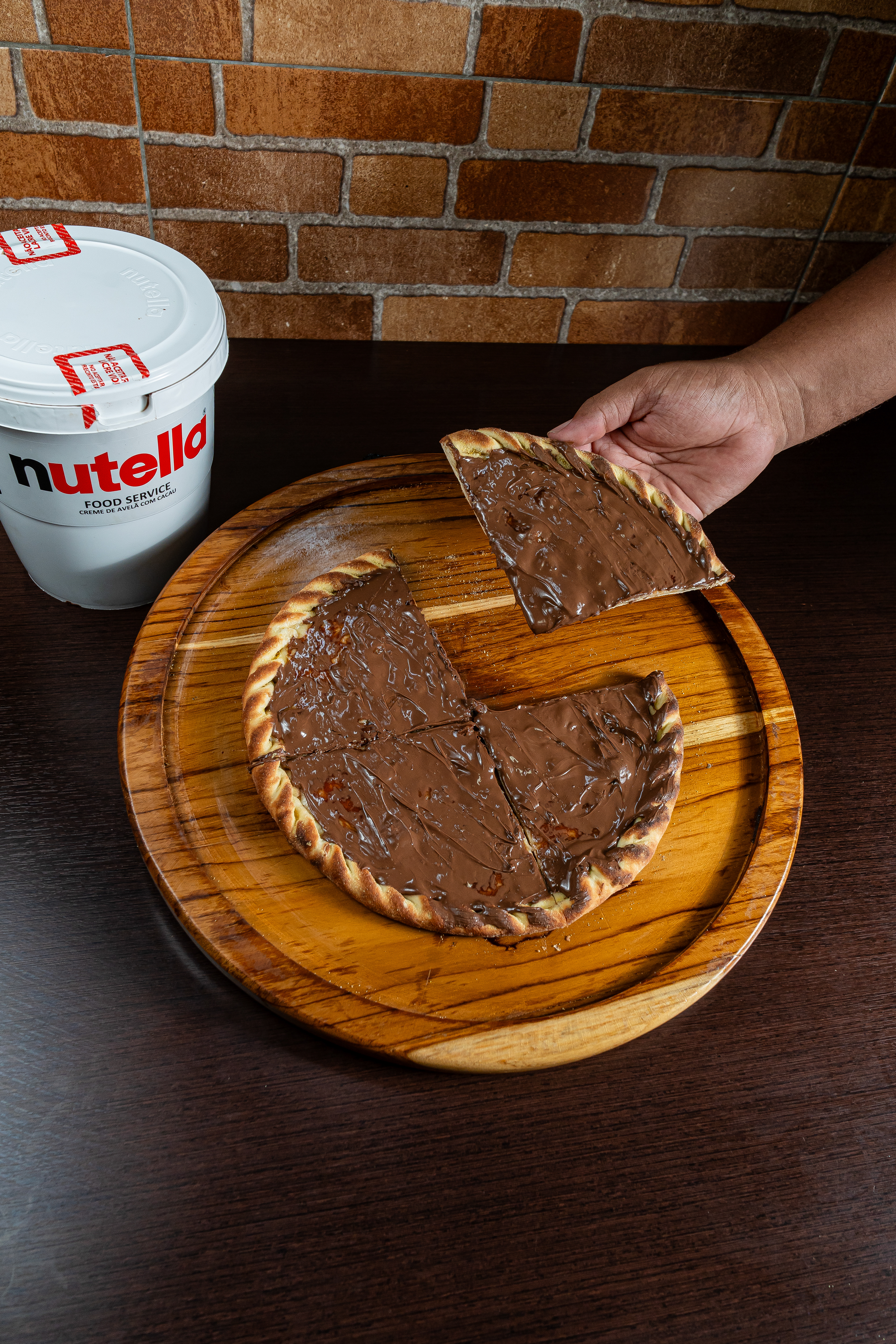 Uma cena que ilumina até os dias mais cinzentos: nossa pizza de Nutella chocolate ao lado de um pote tentador de Nutella. Prepare-se para uma explosão de sabor e felicidade! 🍫✨ #IluminandoComSabor"