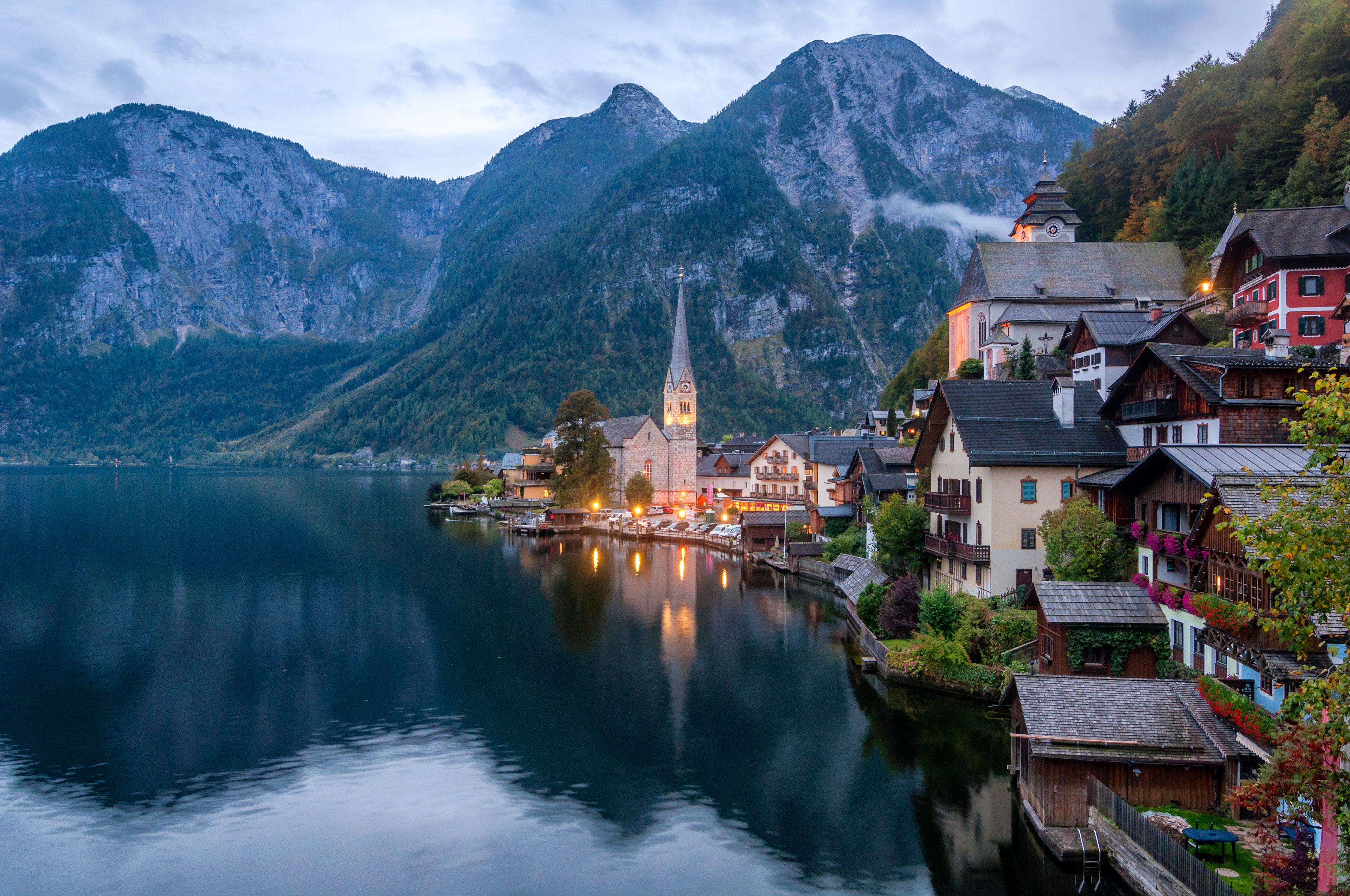 Twilight settles over the alpine village of Hallstatt, casting glassy reflections of the church spire onto the serene waters of Lake Hallstatt.