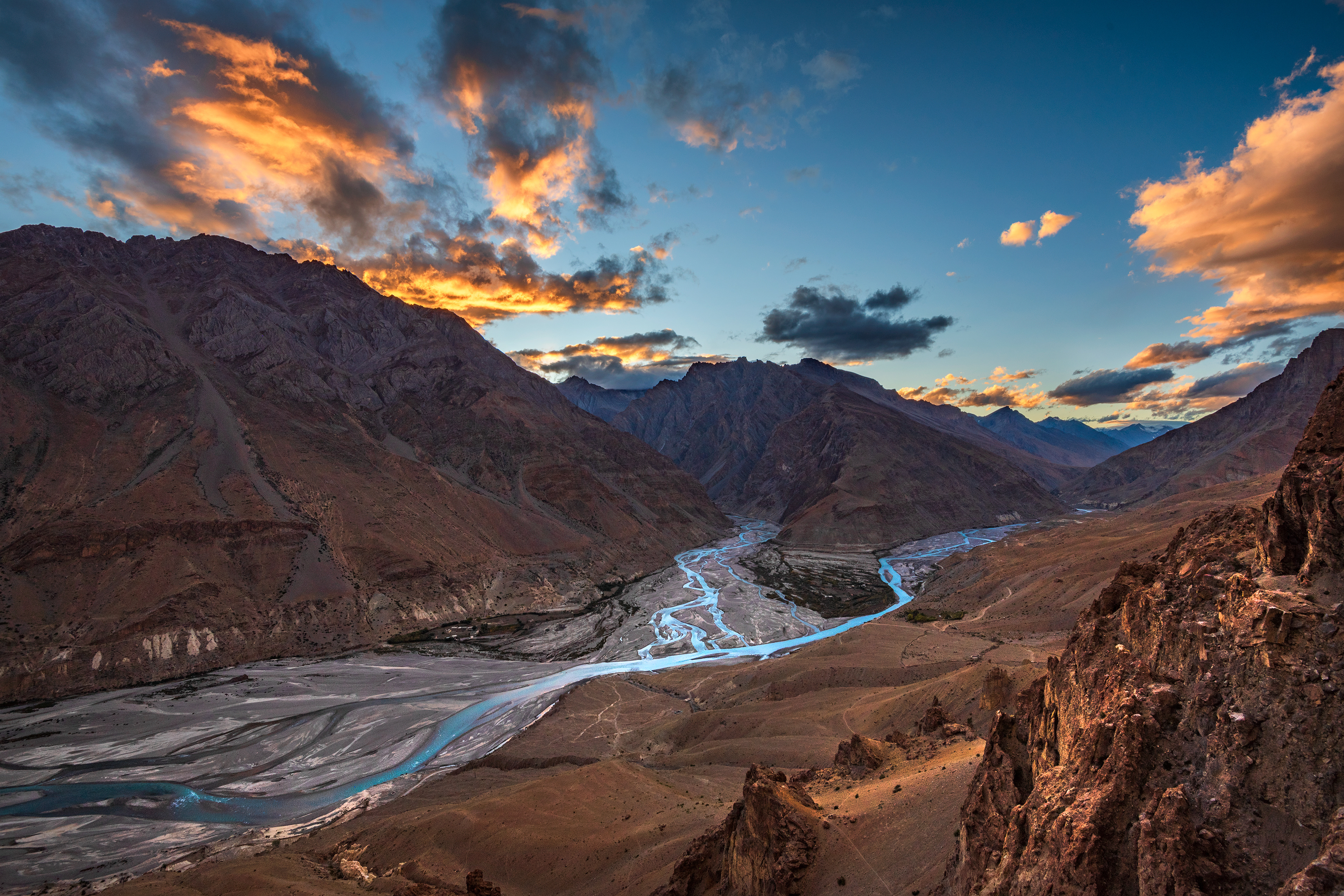 The raw, rugged beauty of the Spiti Valley landscape, where the braided Spiti River cuts through barren mountains under a dramatic sunset sky