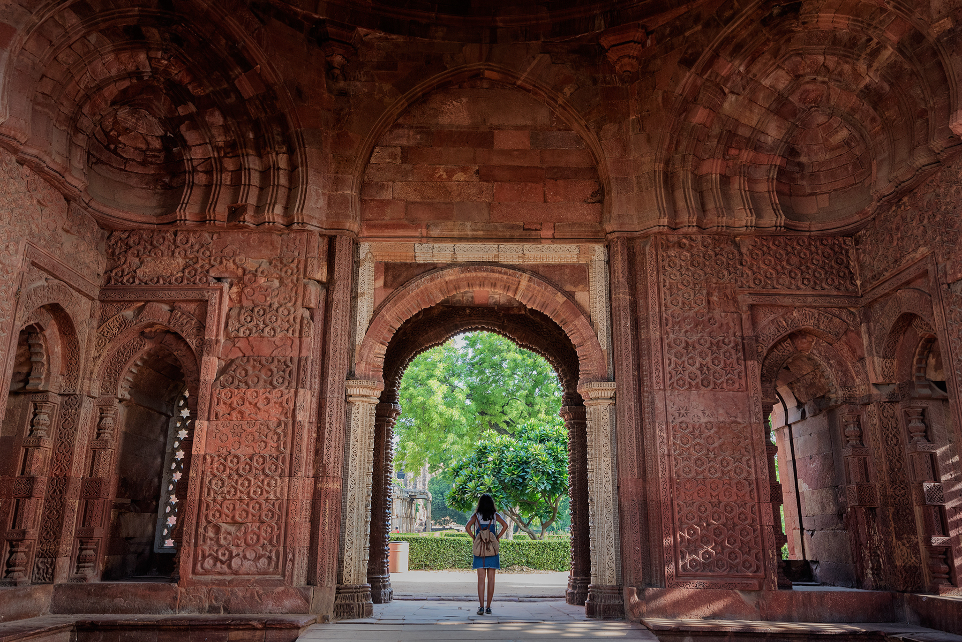Intricate red sandstone carvings frame the view through the Alai Darwaza archway at the historic Qutub Minar complex.