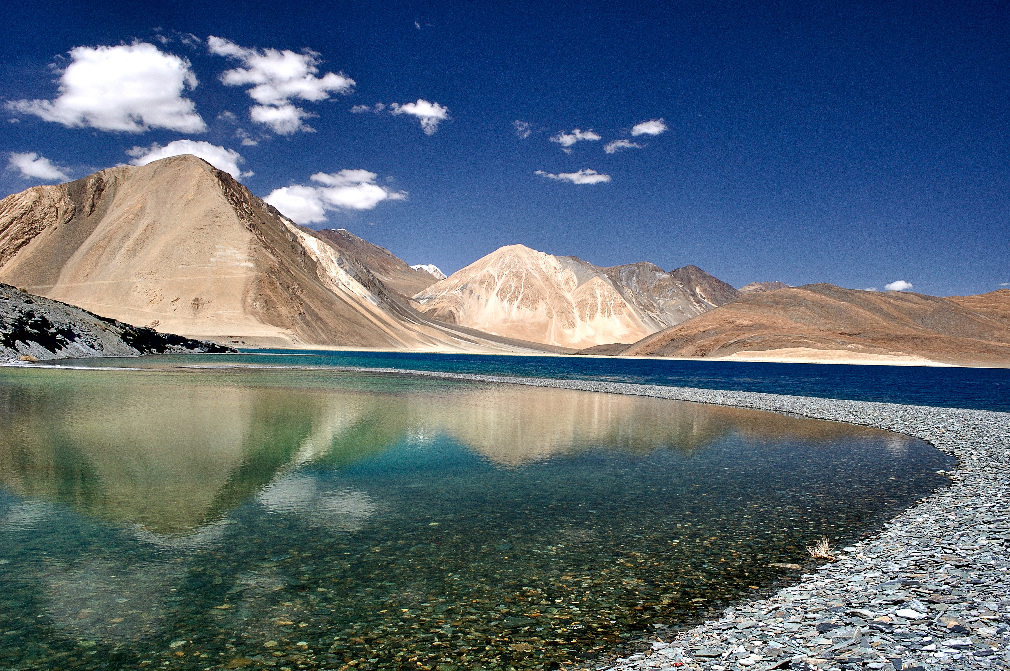 The crystal-clear waters of Pangong Tso reflecting the arid mountains and deep blue sky in perfect symmetry