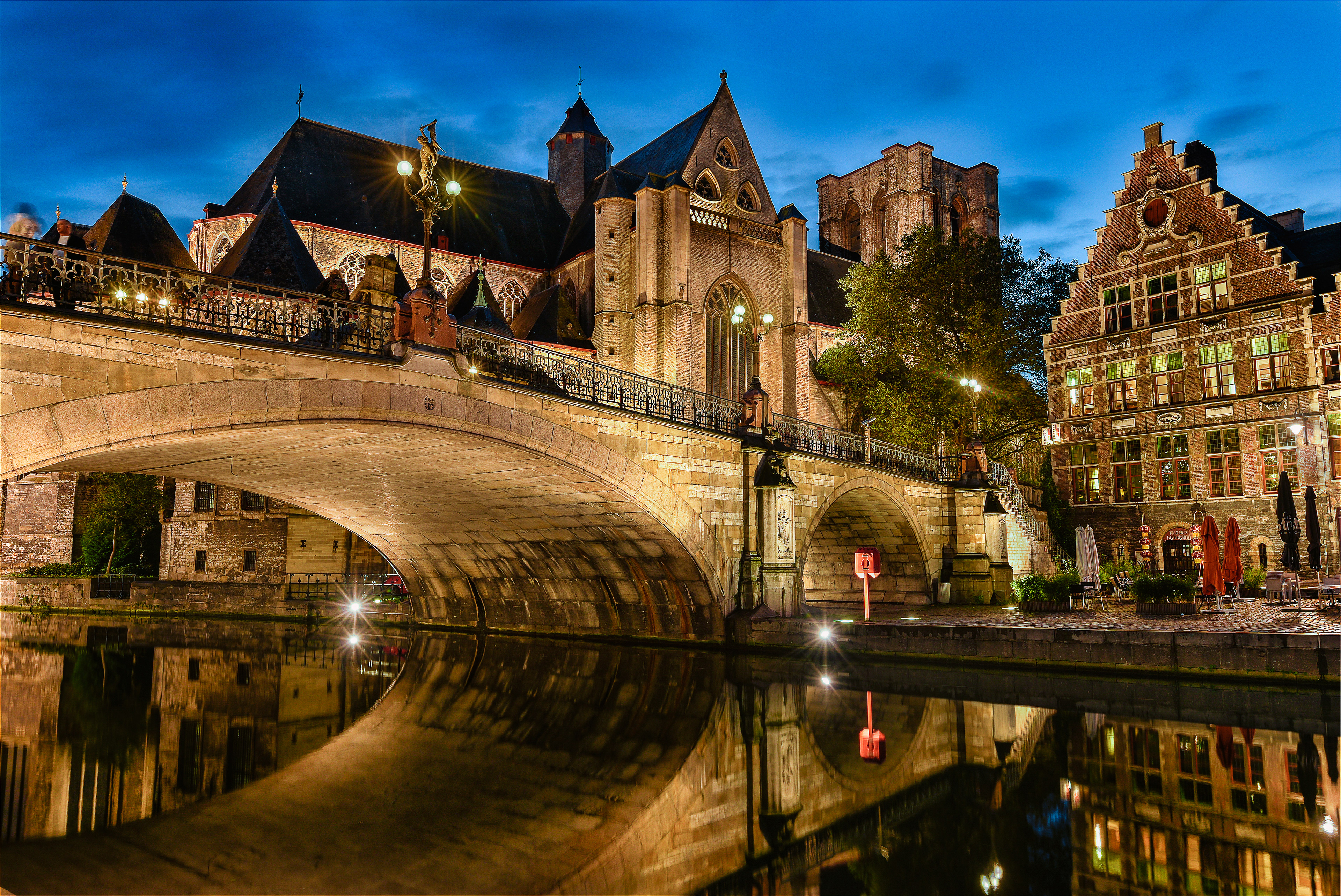 The stone arches of St. Michael’s Bridge reflecting beautifully in the Leie River, surrounded by the medieval guildhalls of Ghent at twilight