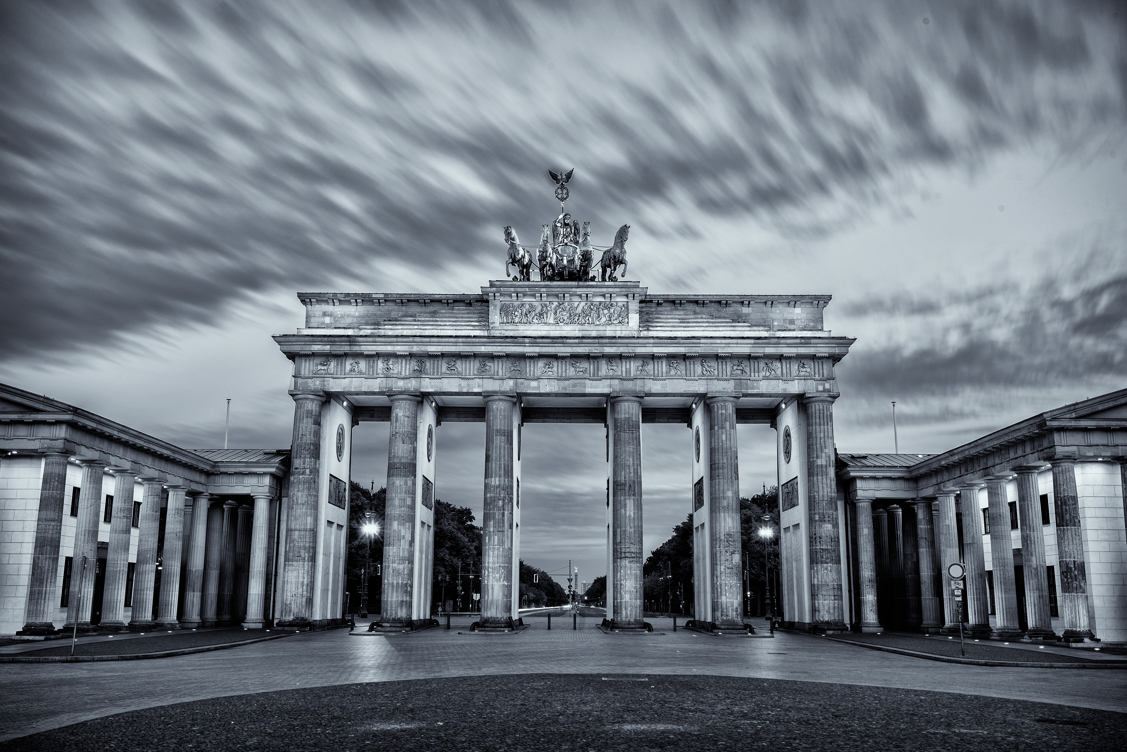 A powerful black and white long-exposure capturing the neoclassical Brandenburg Gate in Berlin under a streak of moving clouds