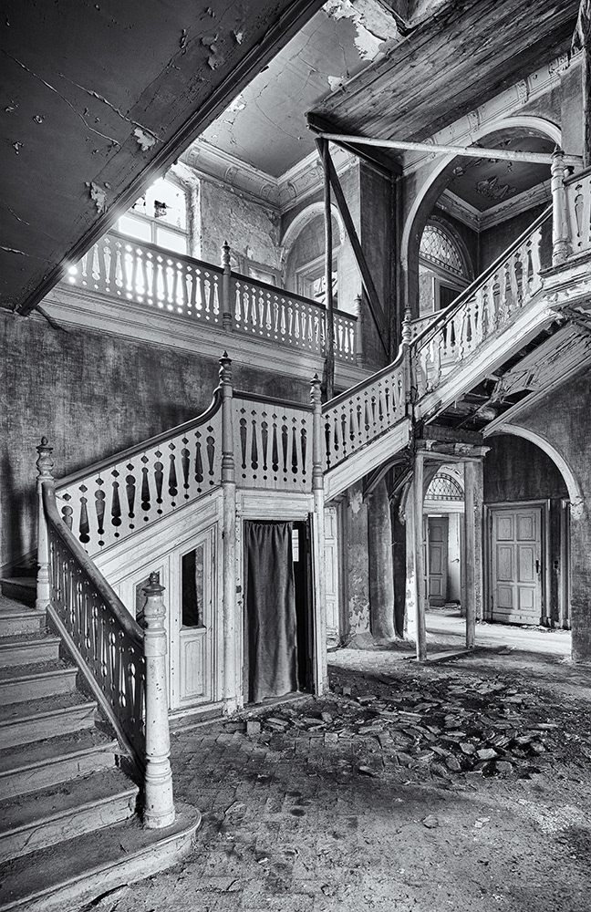 A view into a dilapidated factory owner's villa featuring a staircase that winds steadily upwards, as if seen by M.C. Escher.