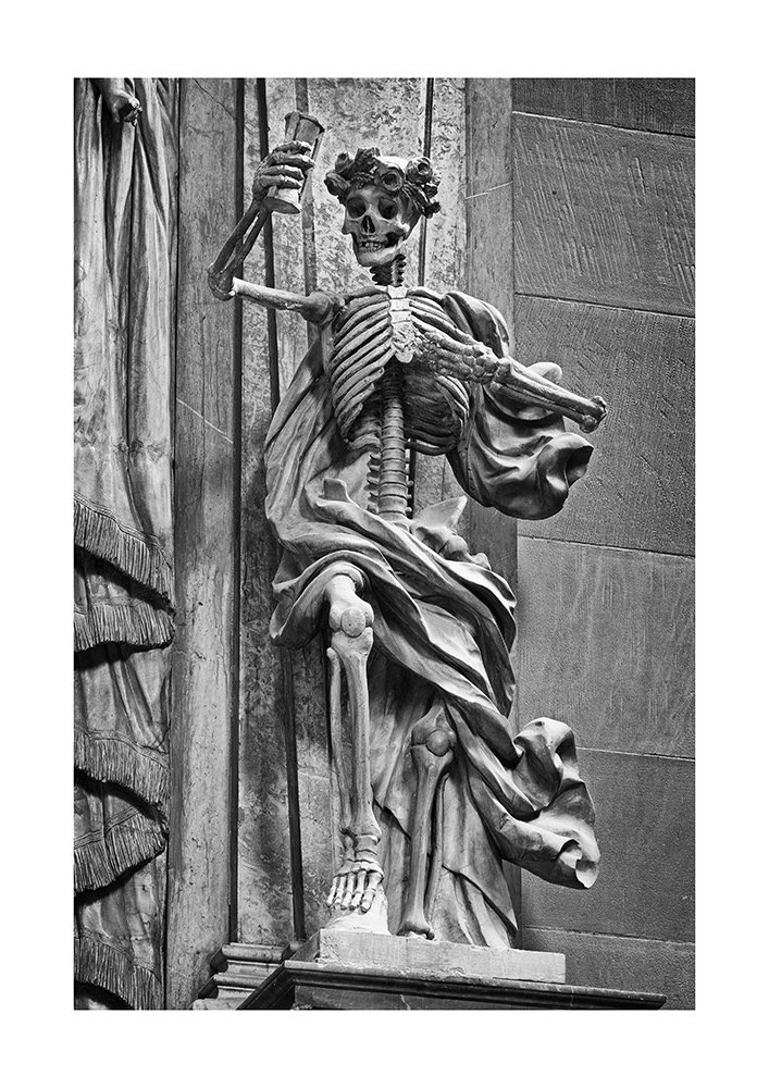 Death, a skeleton in robes, wearing a headdress of roses and ears of grain, holds an hourglass aloft in a warning gesture.