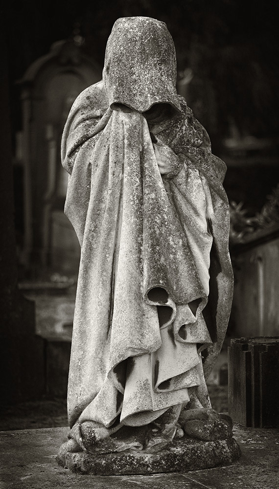 A mourning figure, completely covered by a cloak and hood, with bowed head, in a cemetery in Antwerp.