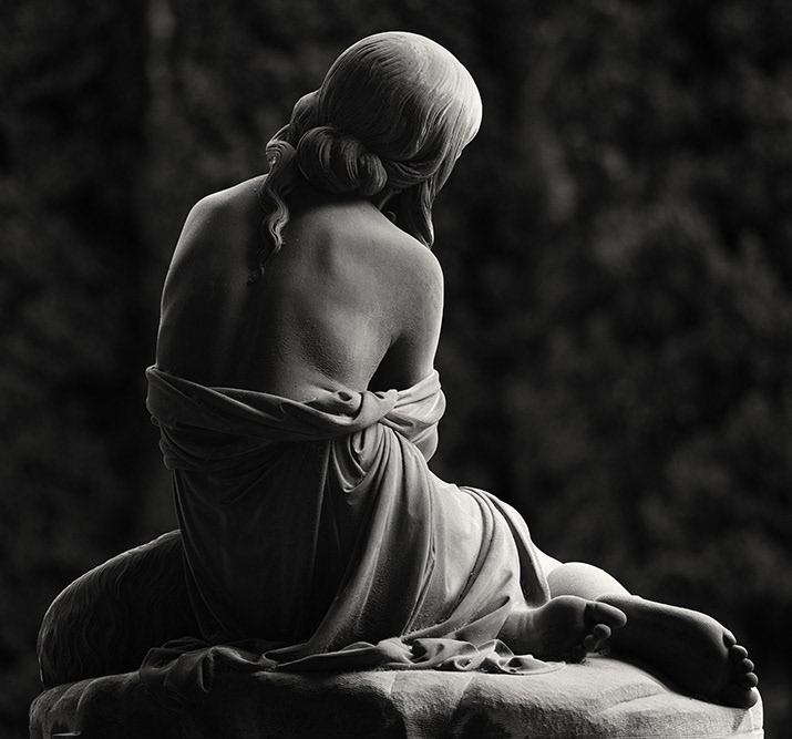 Erotic back view of a young woman sitting on a boulder. The robe is lowered to the hips, the head is tilted to the side.