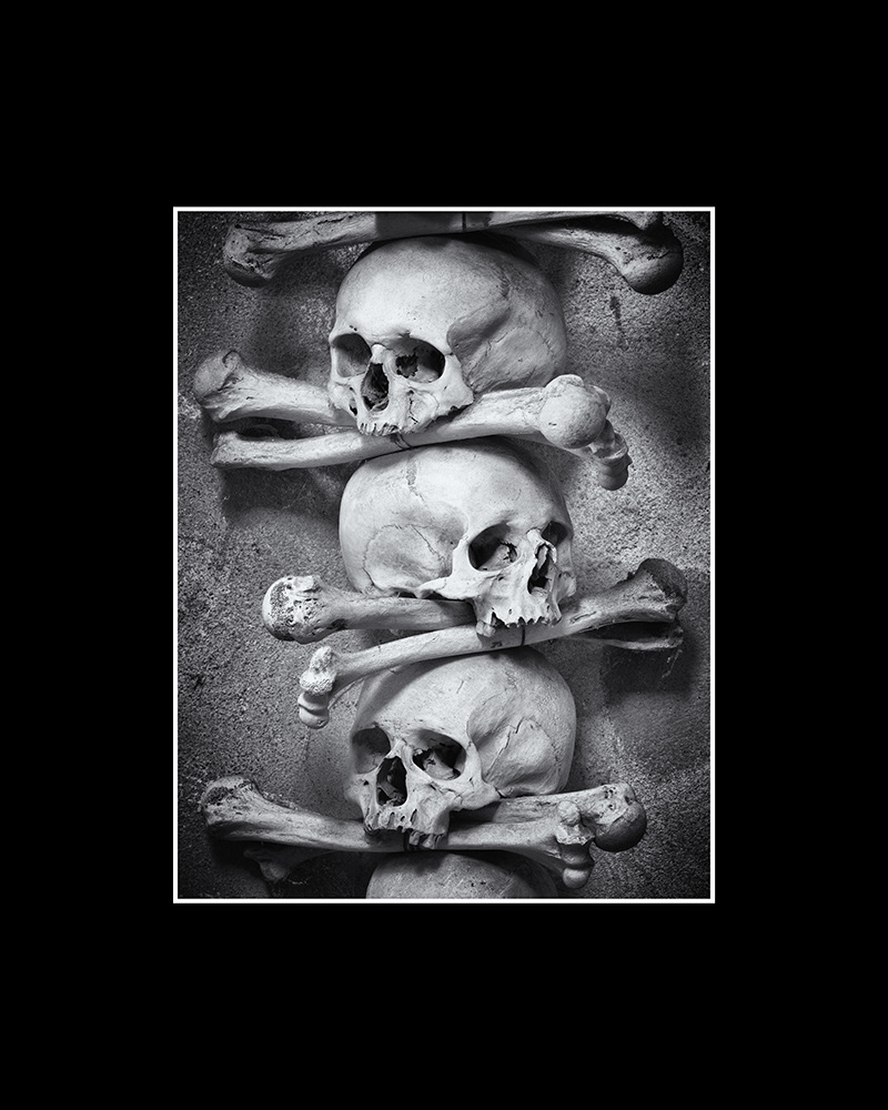 Three human skulls, draped one above the other with crossed bones, form a garland in an ossuary in the Czech Republic.