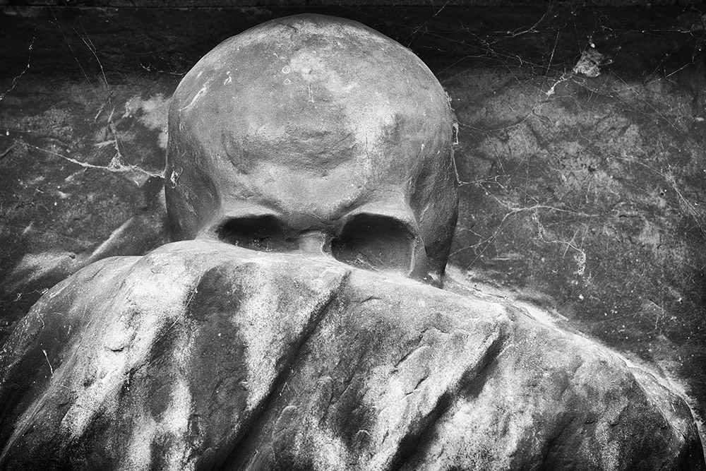 Personified Death stalks us with a sharp gaze from behind his raised robe in a cemetery in Bologna.