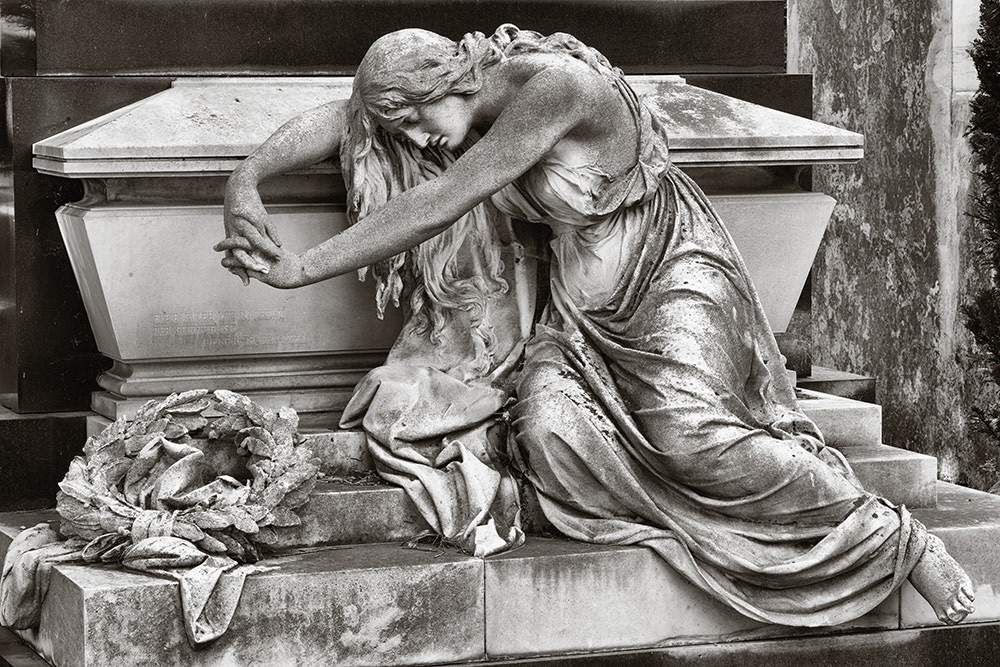 A woman with one shoulder exposed leans against a sarcophagus with her eyes closed, in front of which lies a funeral wreath.