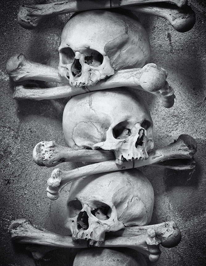 Three human skulls, draped one above the other with crossed bones, form a garland in an ossuary in the Czech Republic.