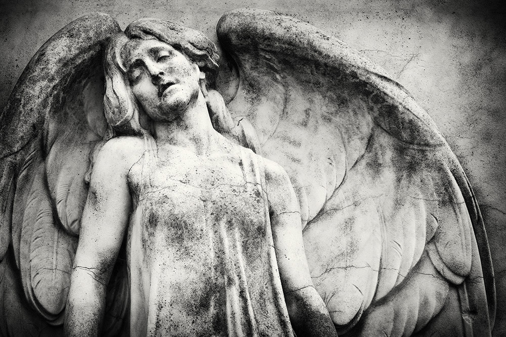 Sculpture of a female cemetery angel with a sad facial expression, large wings, off-the-shoulder robe, morbid charm.