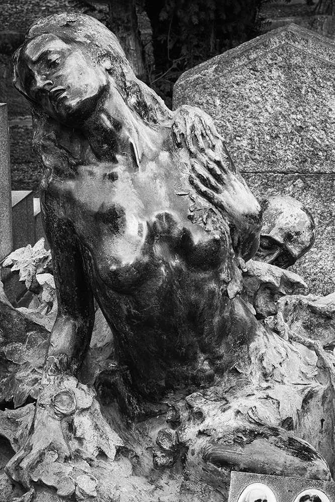A young woman, bare-chested, sits before a tombstone and struggles desperately against Death, who seizes her from behind.