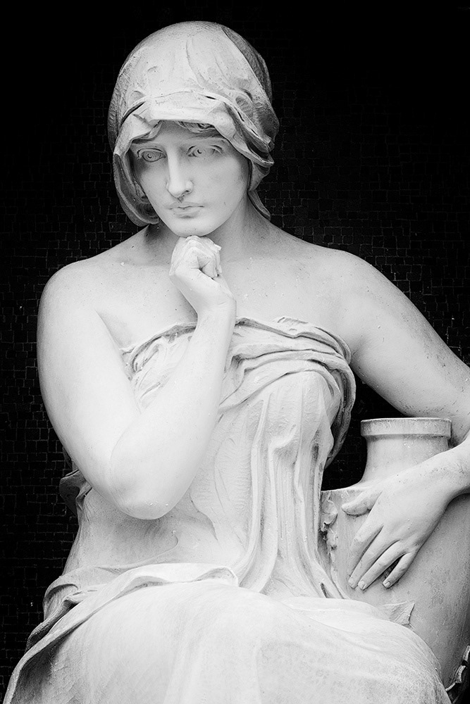 Sculpture of a young woman wearing an off-the-shoulder dress holding an urn and looking pensive. Very tender and erotic.