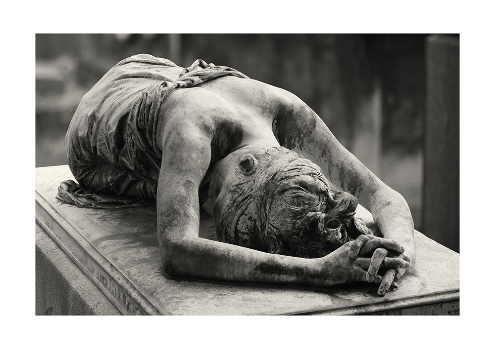 A slender young lady lies with her shoulders bare on the lid of a sarcophagus in a Parisian cemetery.