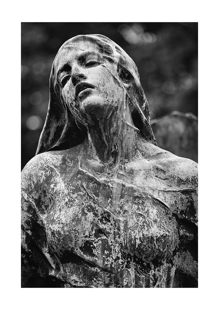 Bronze sculpture of a young lady in a Parisian cemetery, half-closed eyes, slightly open mouth, covered in patina.