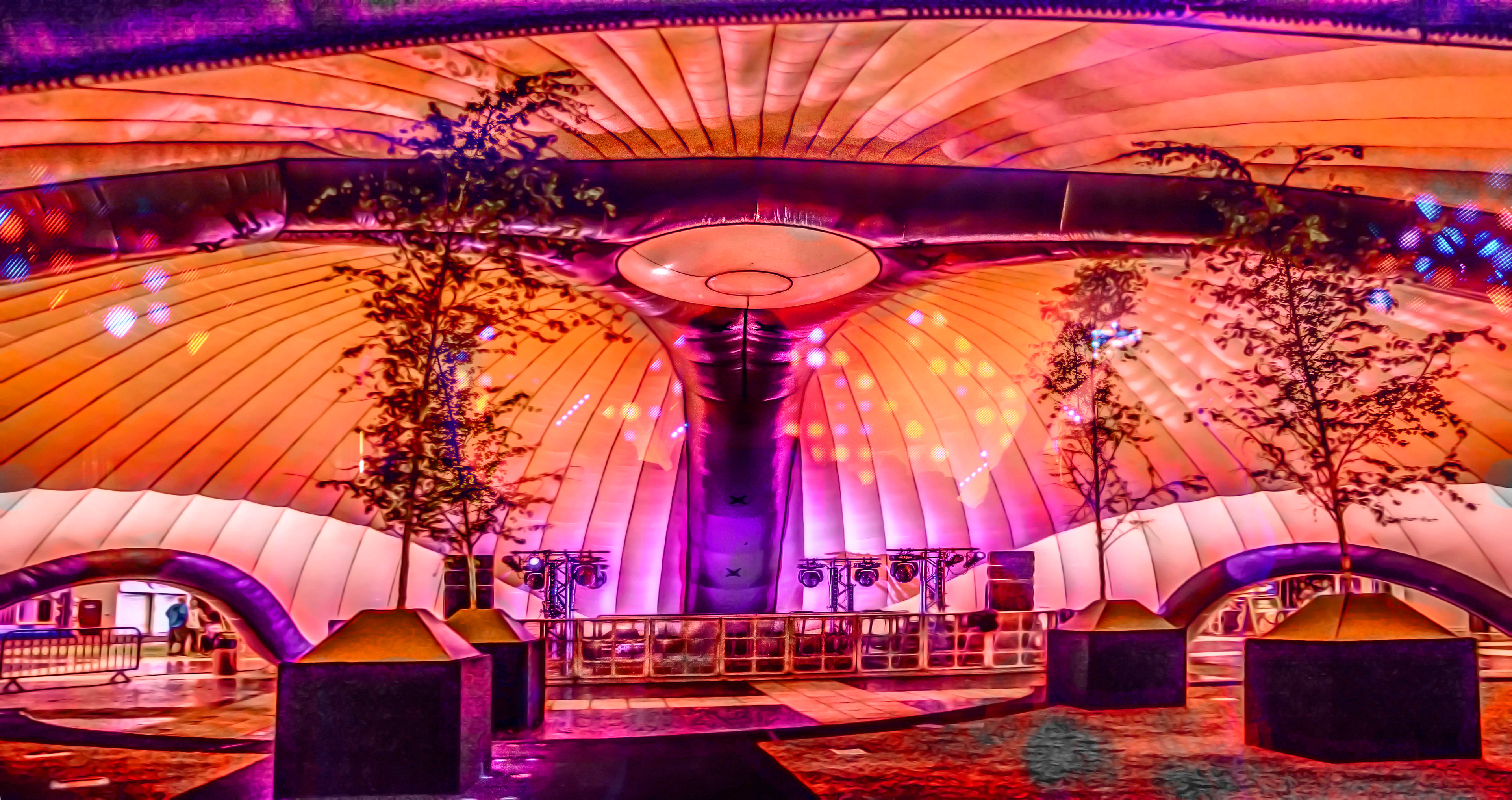 Vibrant, pink-lit interior of a modern venue with an inflated dome ceiling, trees in planters, and spotlights, creating a lively, futuristic ambiance.