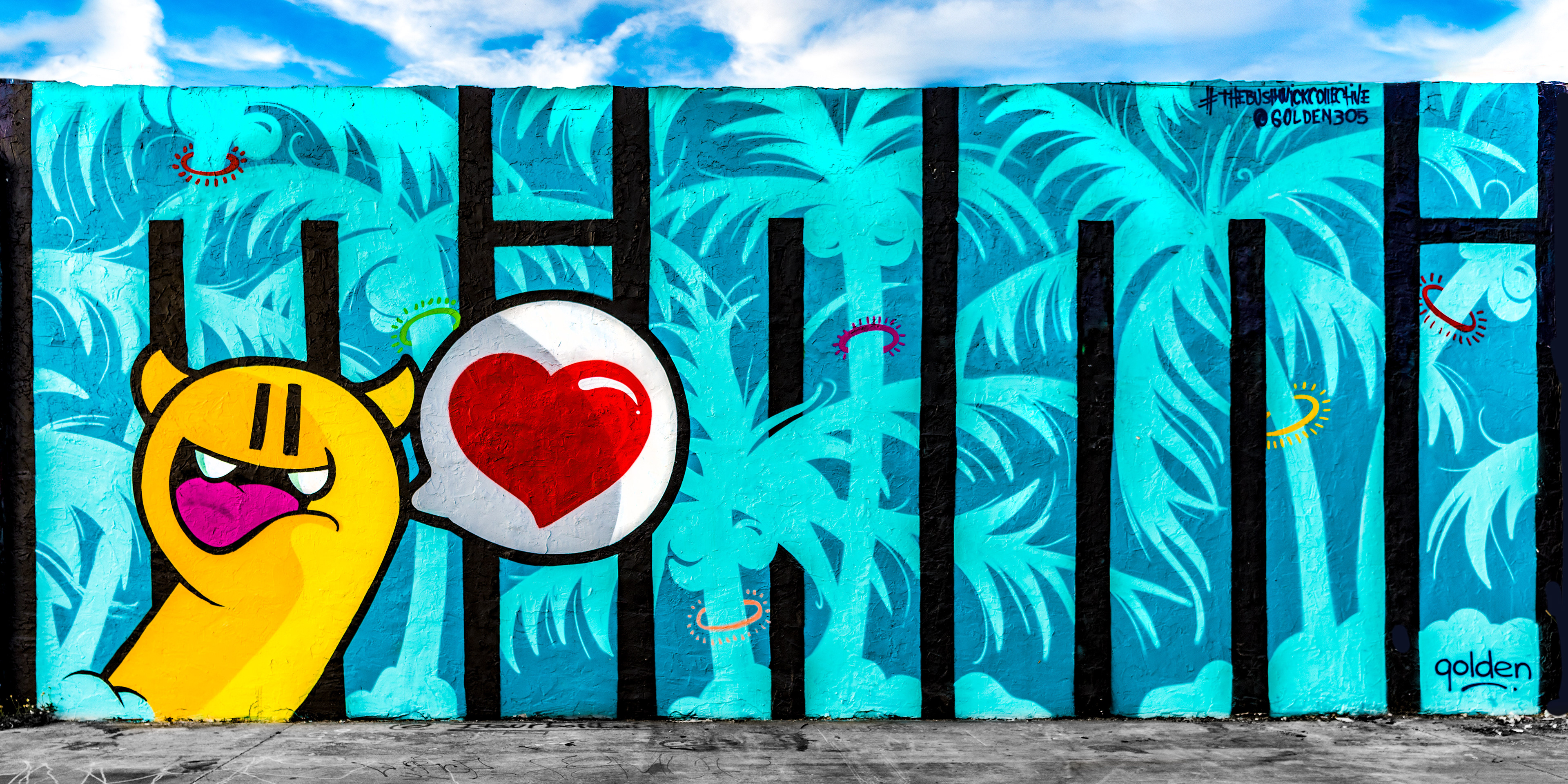 Graffiti mural with a yellow cartoon character holding a red heart on a speech bubble. Blue tropical background with black vertical bars and colorful accents. Birmingham Photographer, West Midlands