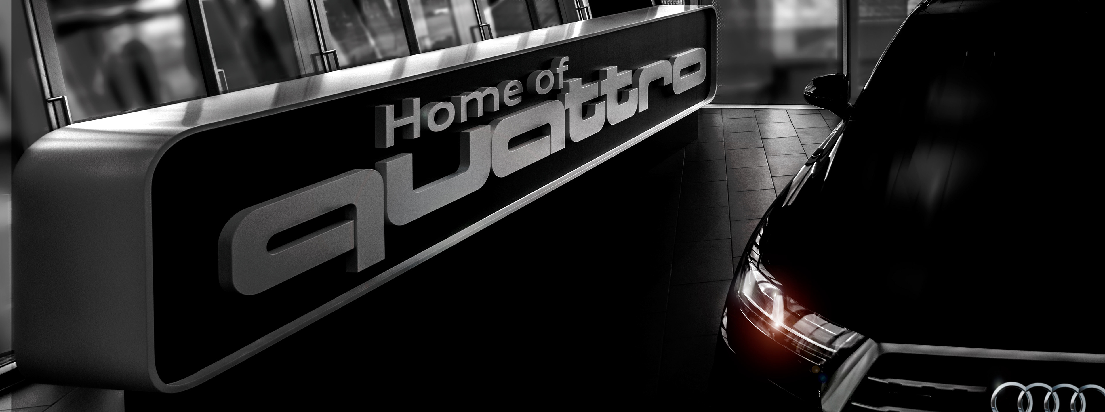 Dimly lit showroom with illuminated "Home of quattro" sign and a sleek car's headlight partially visible, conveying luxury and sophistication.