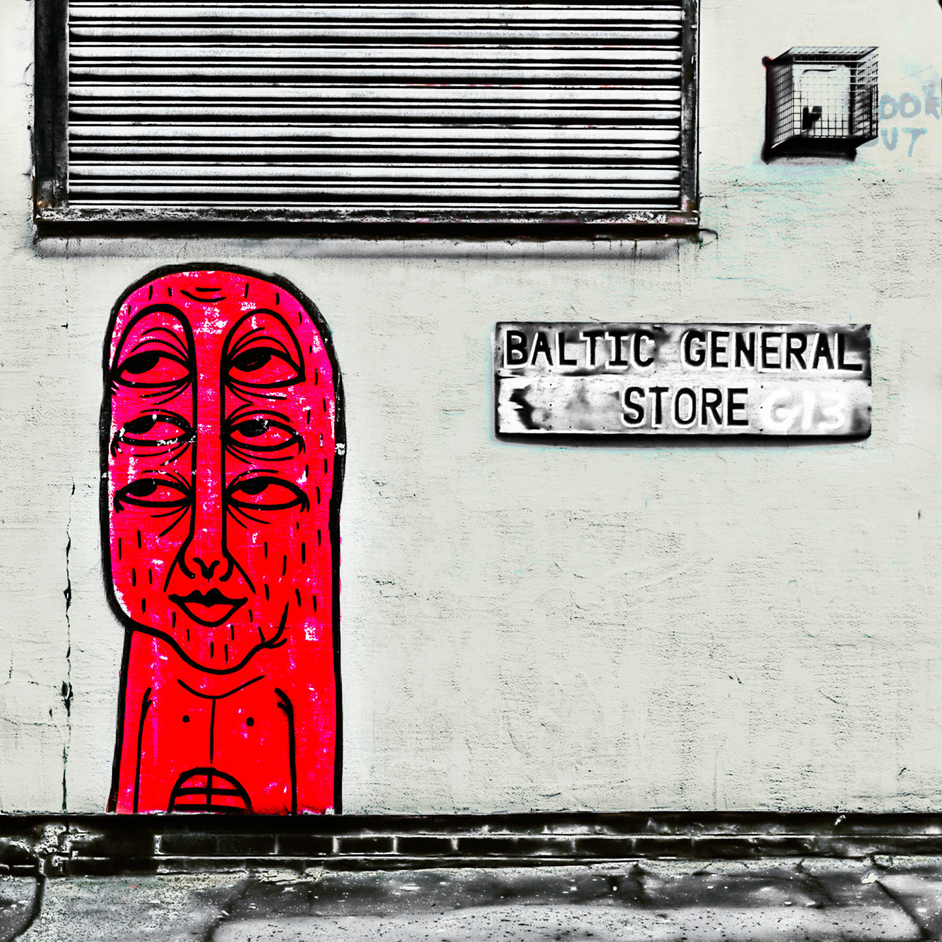 Street art shows a red, multi-eyed face painted on a textured wall next to a worn "Baltic General Store" sign. The tone is urban and edgy. street art during Liverpool Disco Festival