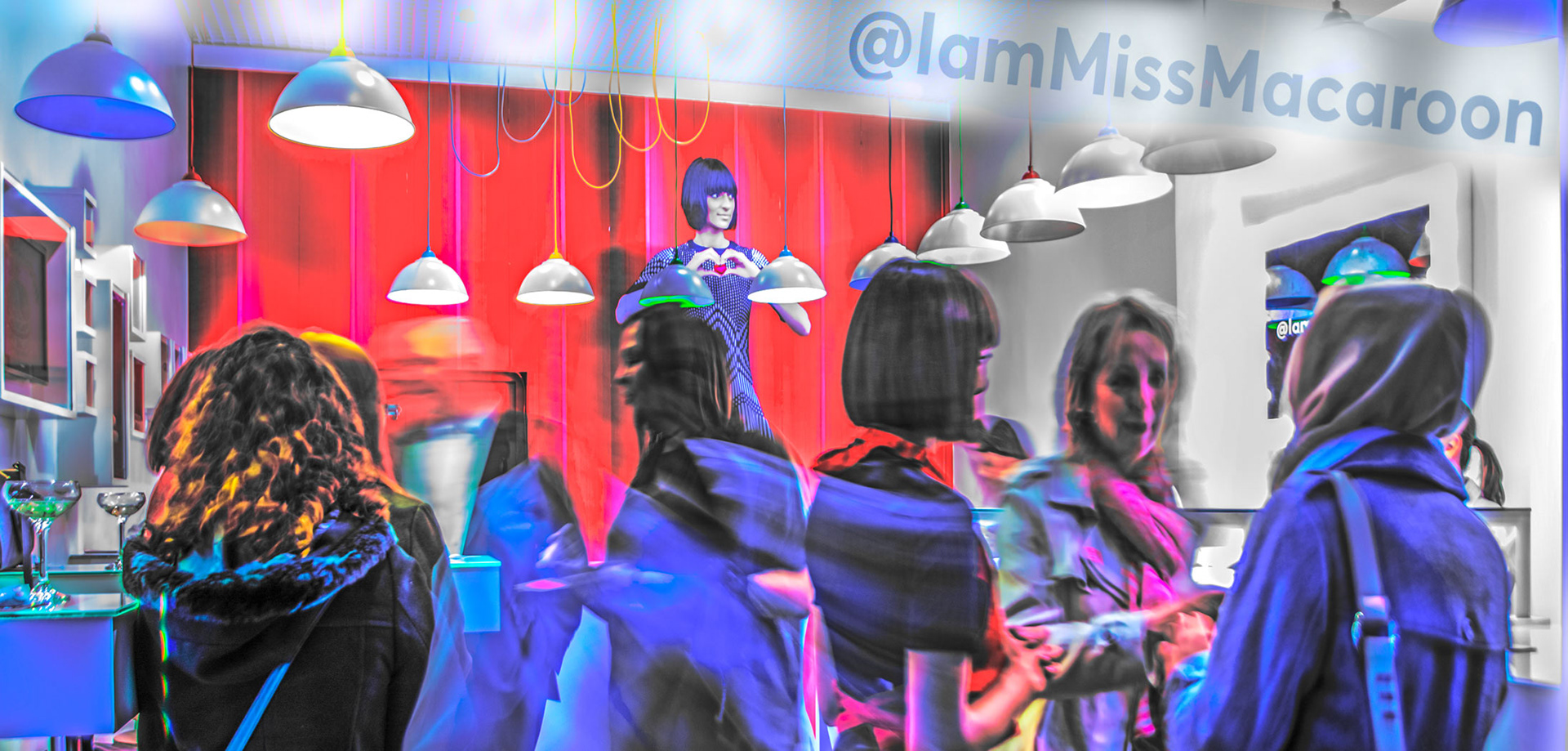 A vibrant scene with people gathered in front of a red curtain. Bright, colorful lighting creates a lively atmosphere. Hanging lamps add modern flair.