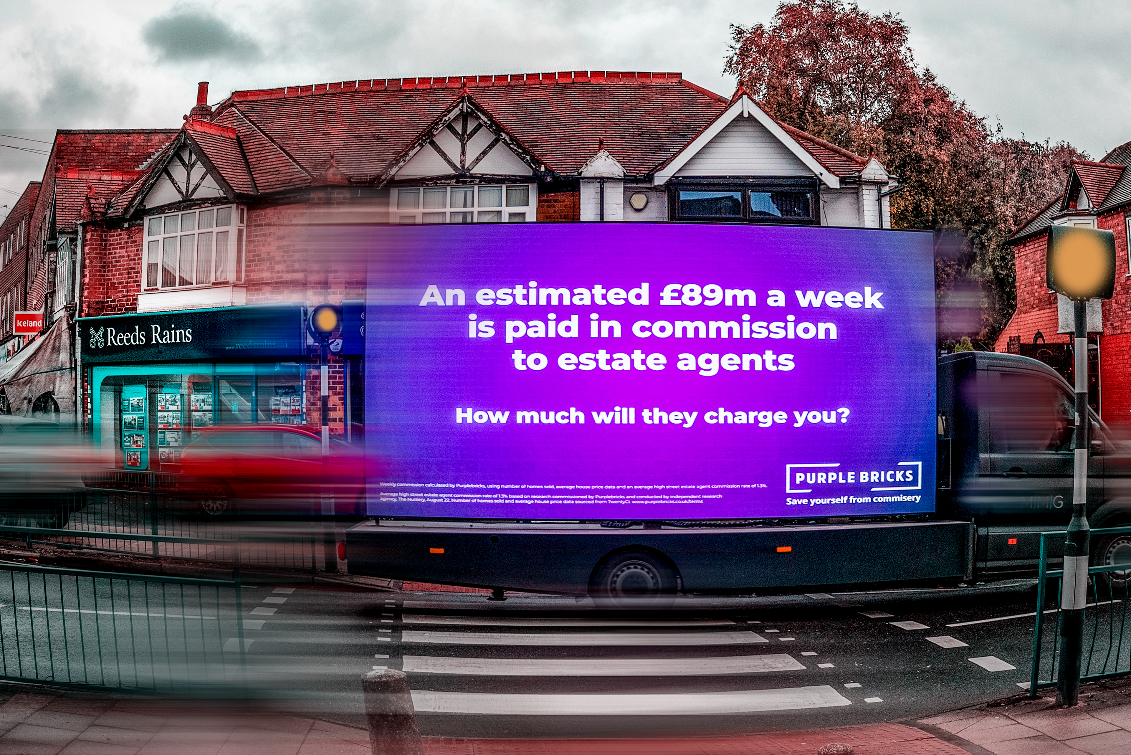 A large purple billboard on a truck reads, "An estimated £89m a week is paid in commission to estate agents. How much will they charge you?" It parks beside a red-brick building on a busy street, conveying a message of cost-awareness. Photography Yardley Birmingham