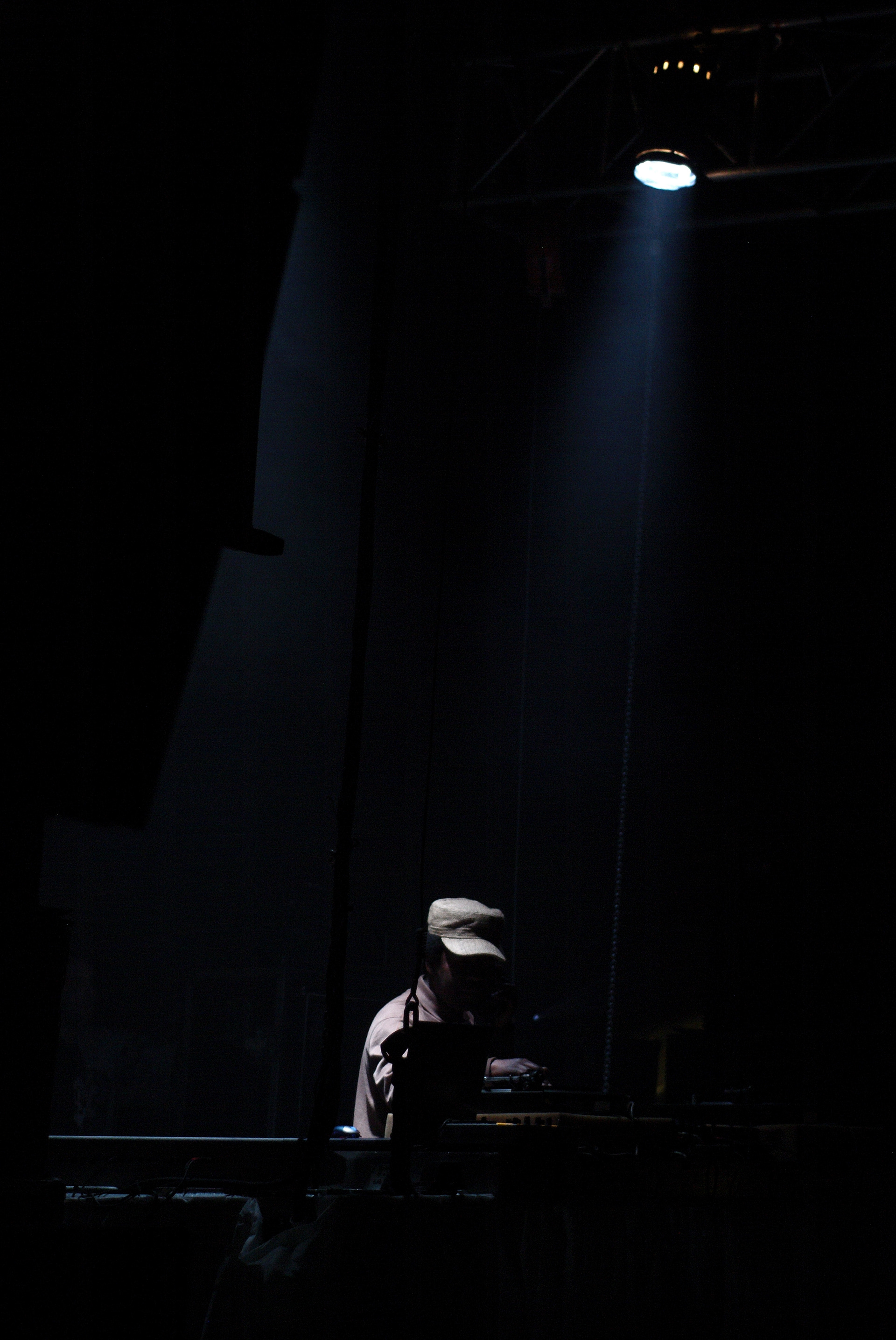 Silhouette of DJ Norman Jay MBE wearing a hat, DJing in a dimly lit space. They are using music equipment, creating a mysterious, focused atmosphere.