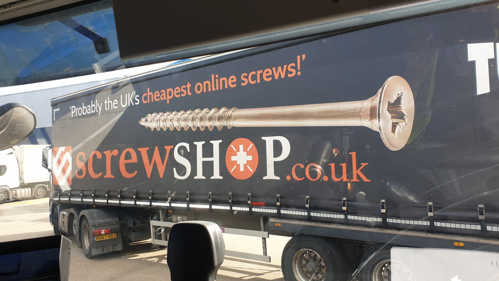 Truck with side advertisement featuring a large screw image and text: "Probably the UK's cheapest online screws! screwSHOP.co.uk." Positioned at a loading area.
