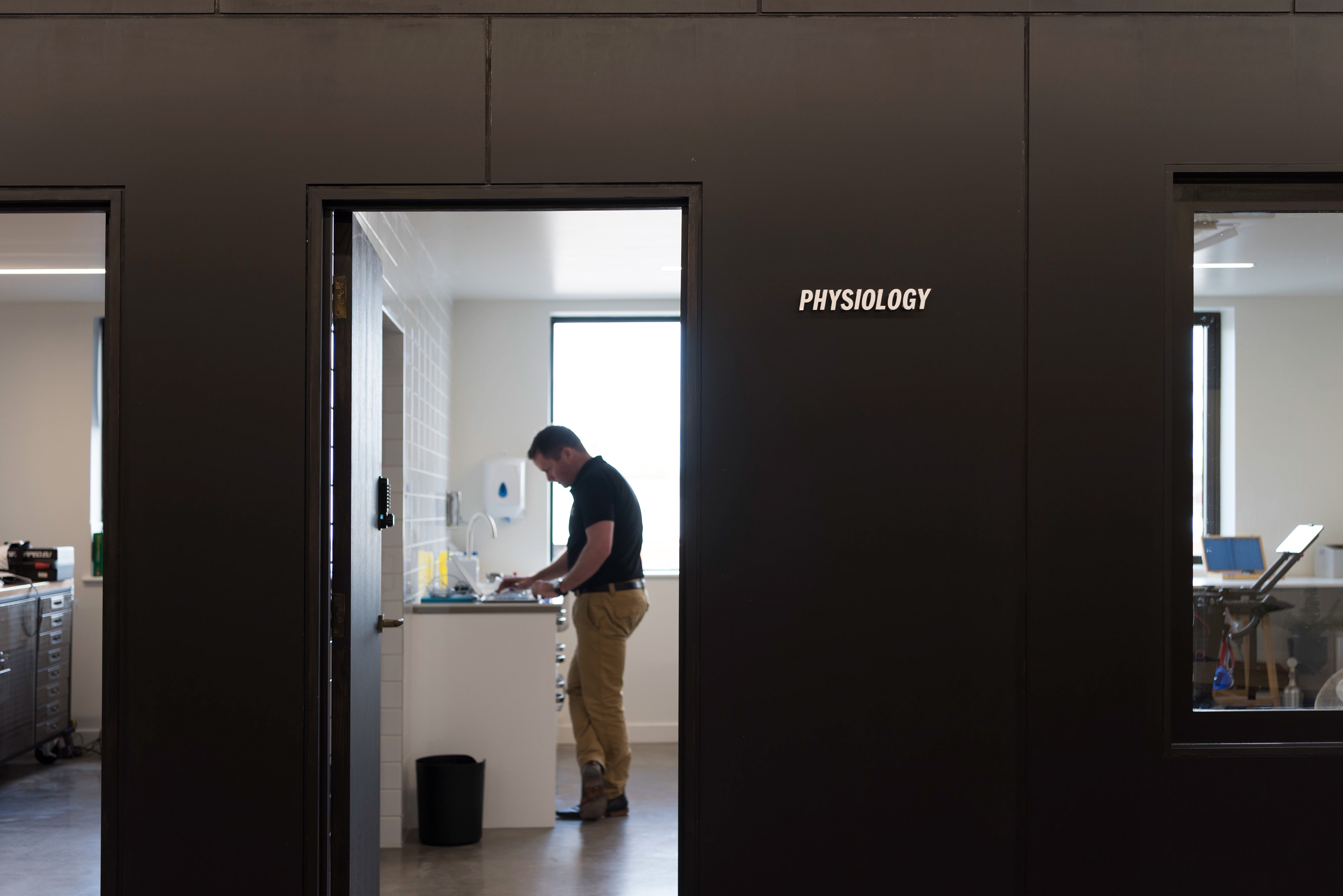 A person stands inside a room labeled "Physiology," focusing on a sink. The space is well-lit and orderly, conveying a sense of concentration and study.