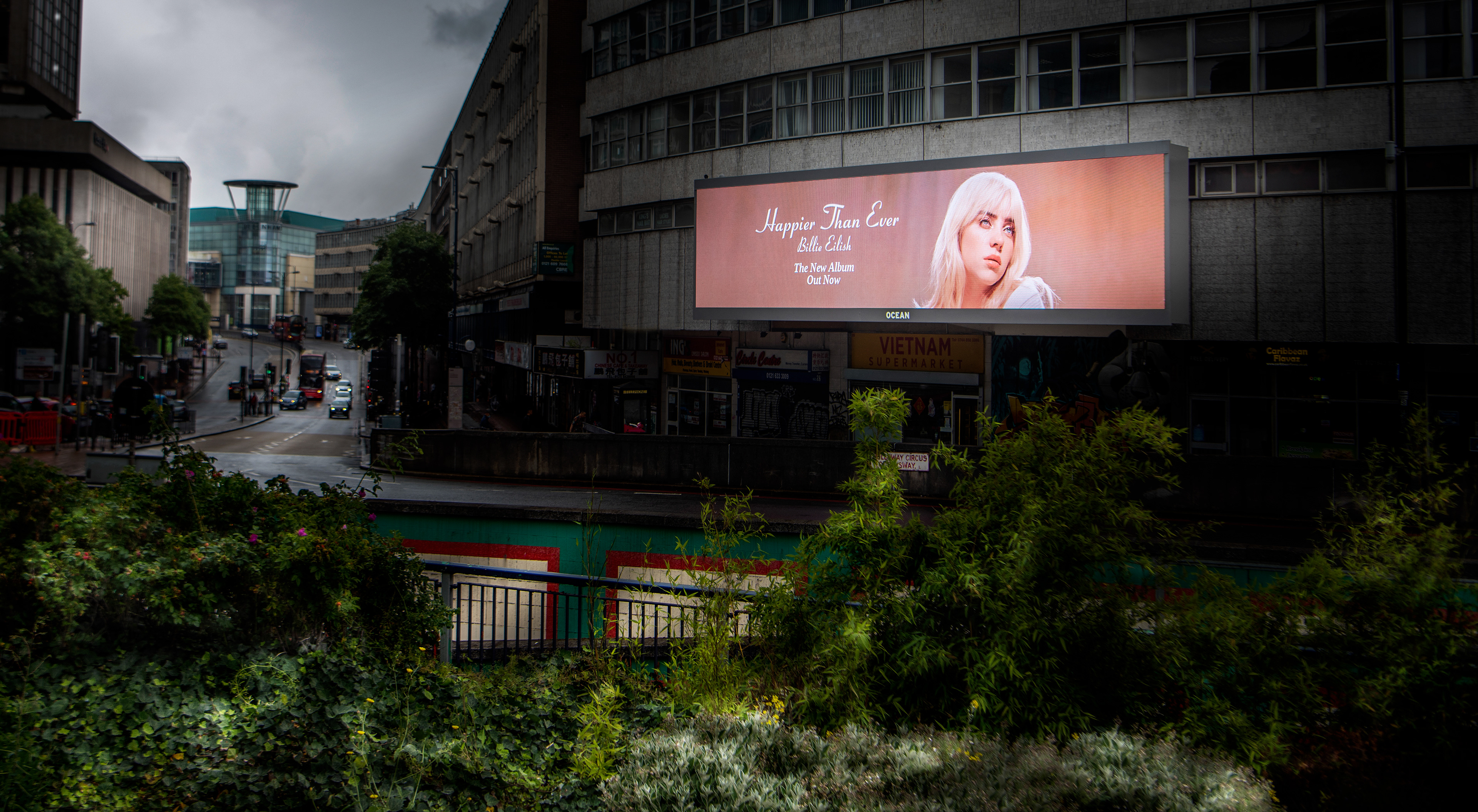 Billboard on a city street features an album ad depicting a blonde woman against a bright backdrop. It's a rainy, overcast day with empty sidewalks. Digital signage photographer Birmingham