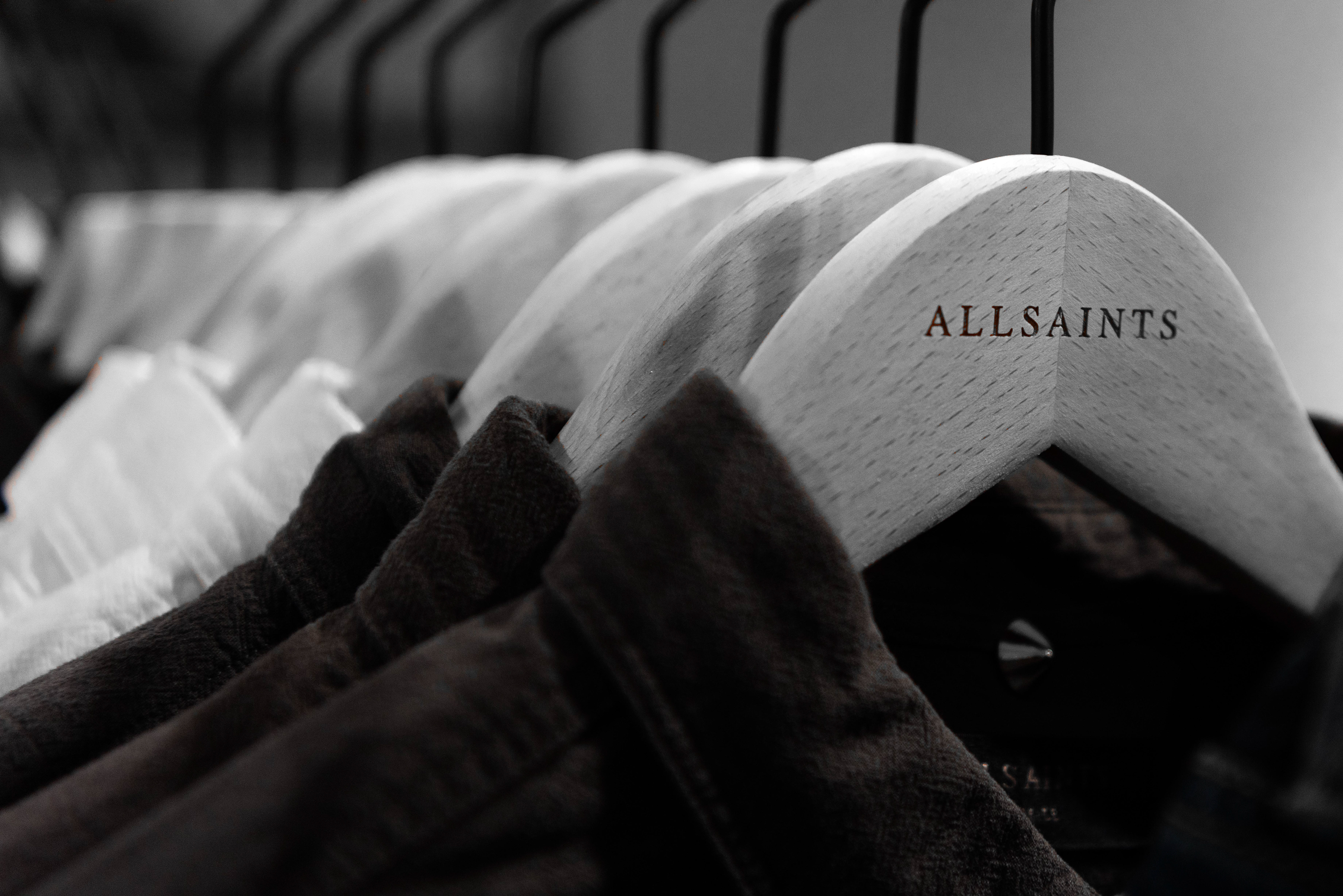 Chic clothing store display of AllSaints hangers holding white and dark shirts, creating a minimalist and stylish atmosphere.