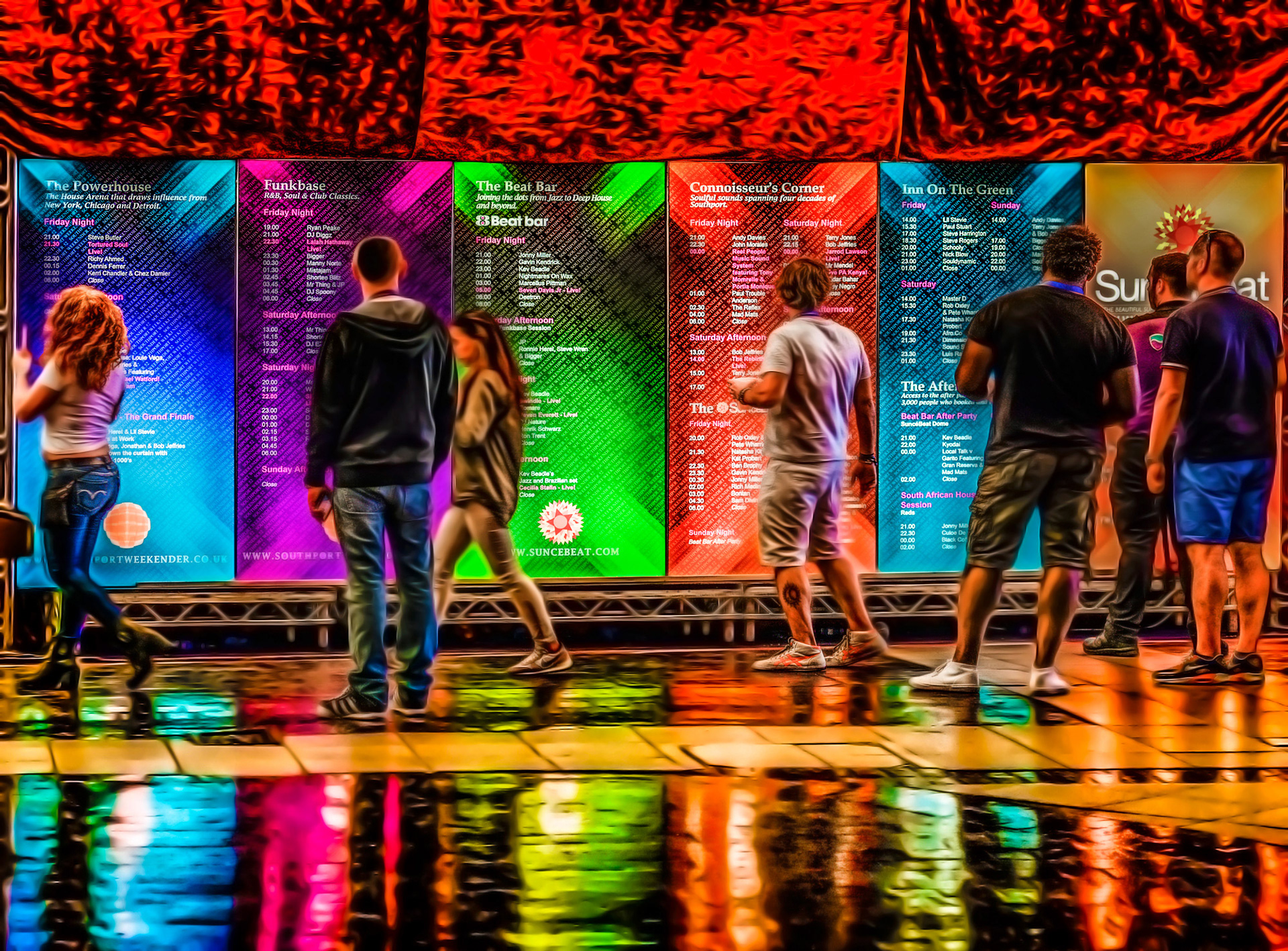 People stand in front of vibrant event schedule panels with vivid colors, reflecting on a glossy floor. The atmosphere is lively and dynamic.