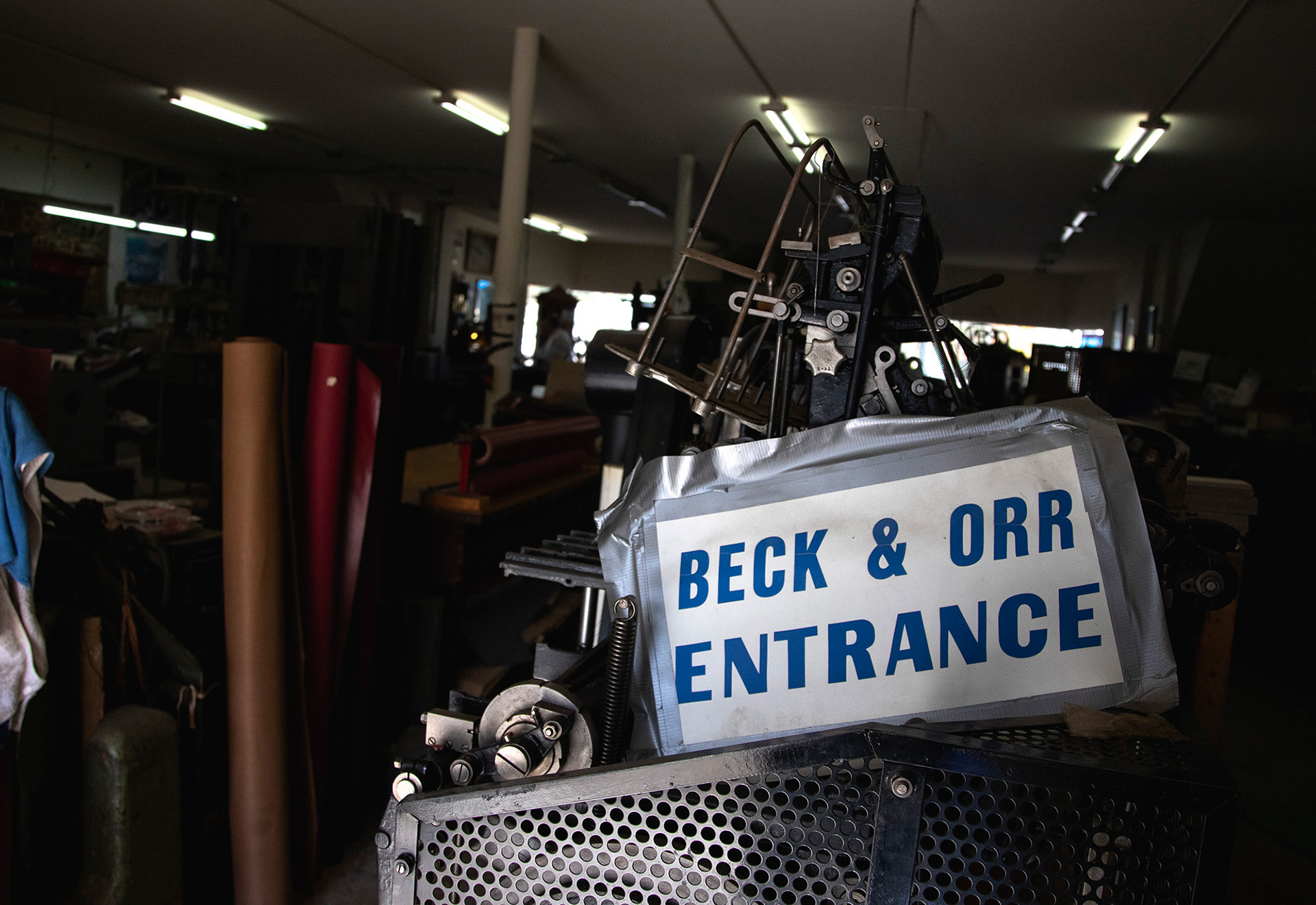 A sign at the back entrance to Beck and Orr that often goes unnoticed welcomes customers in as it is stacked upon rolls of paper and a machine that goes unused. This sign may once have been on the front door, but now is right inside a garage door that opens up and is mostly only used by Ron and Skip Bowman.