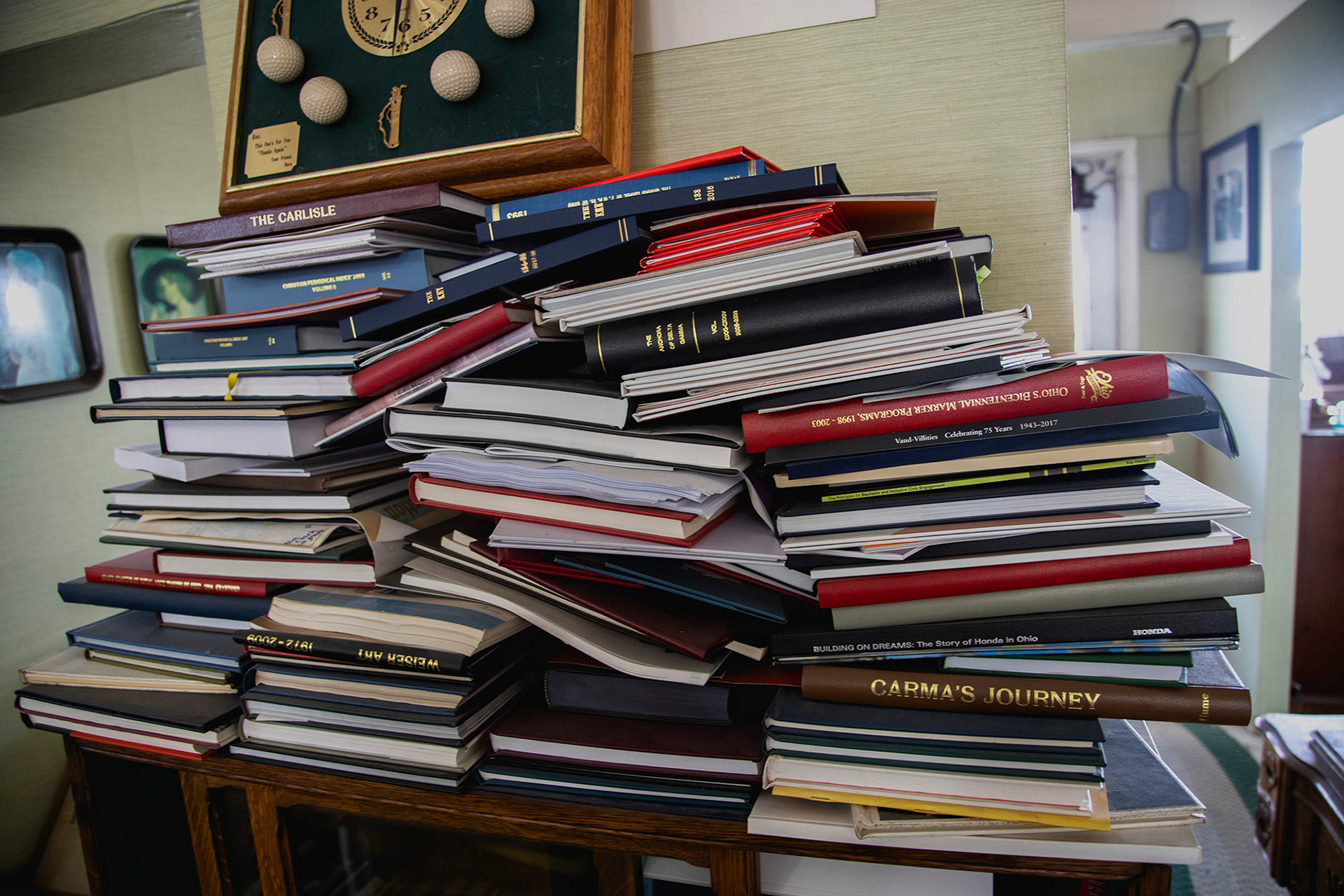 A stack of finished books that have gone unsold or not picked up sits against a wall near the table with the finished products of rebound antique books. Customers have 15 days to pick up products before they are relinquished to the store.