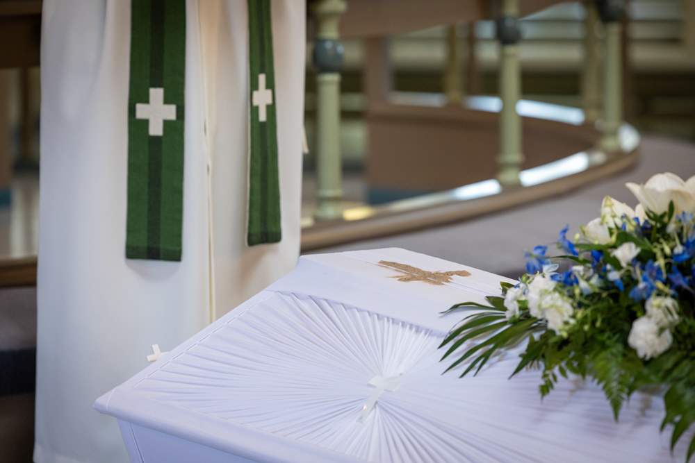 Hautajaiskuvaus esimerkkikuva. Lähikuva arkusta, jonka päälle on piirretty hiekalla risti.