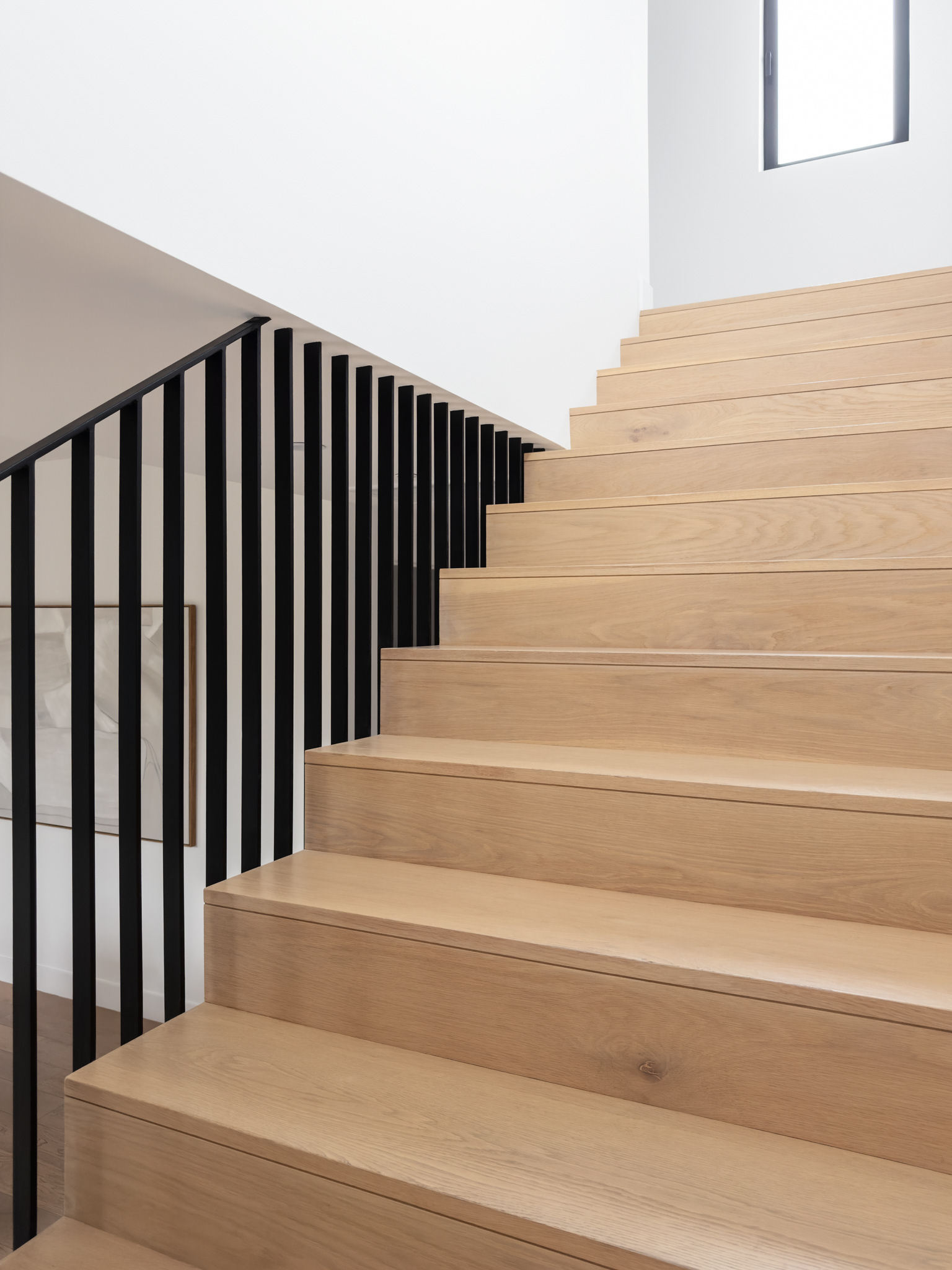 Modern staircase featuring light wood treads, minimalist black metal railings, white walls, and abundant natural light.