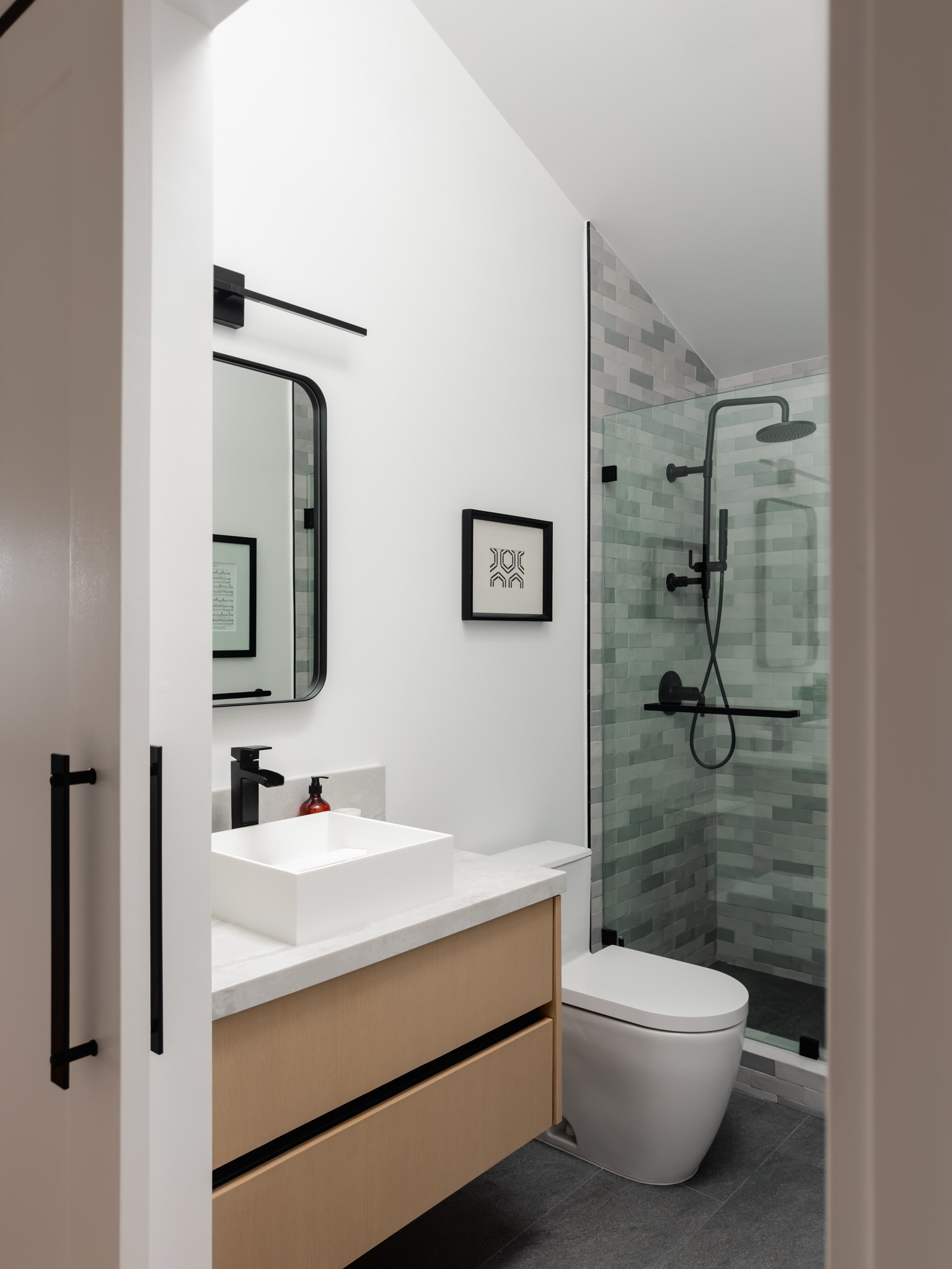 Modern bathroom featuring a floating wood vanity, vessel sink, black fixtures, glass-enclosed shower, and soft gray tile.