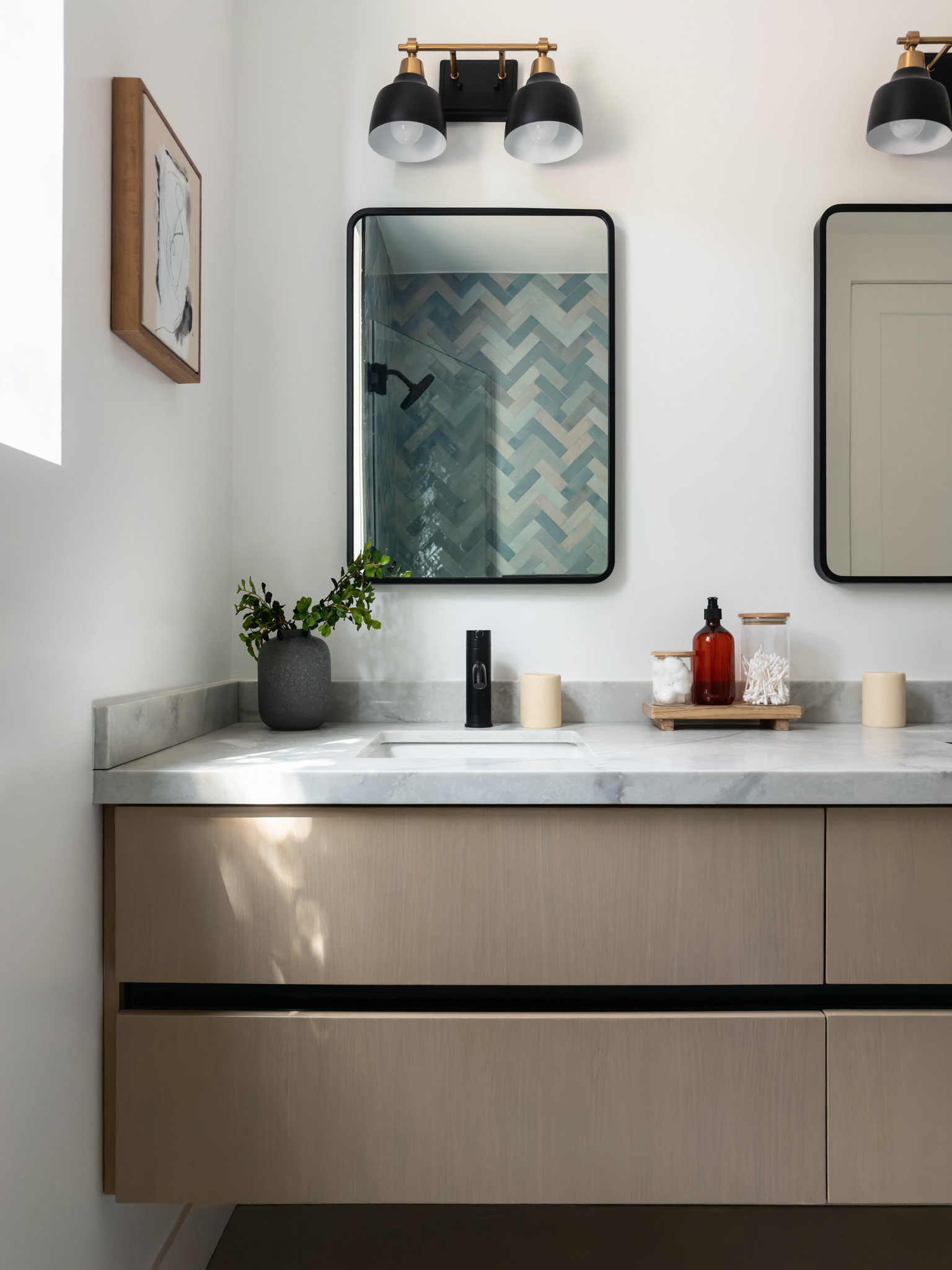 Modern bathroom vanity with custom wood cabinetry, marble countertop, black-framed mirrors, and contemporary brass and black lighting.